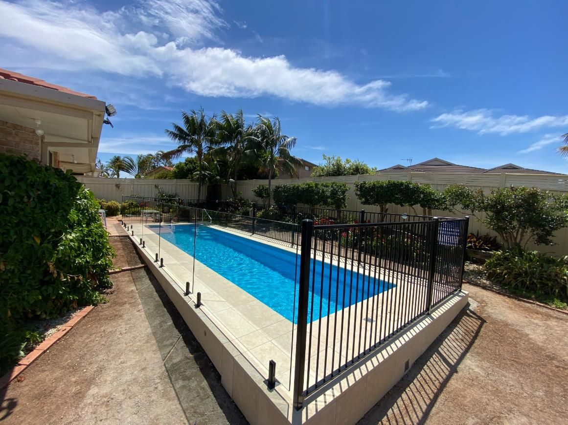 A Large Swimming Pool With A Black Fence Around It — Glass Pool Fencing Australia in Old Bar, NSW