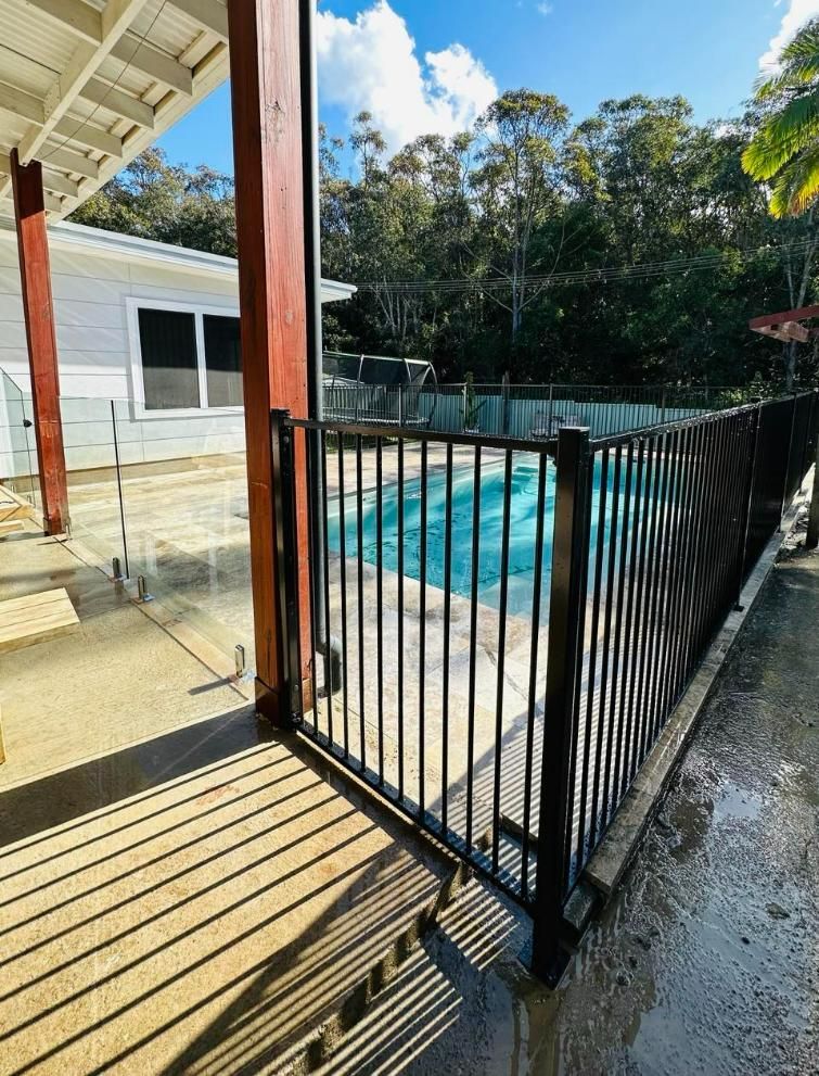 A Fence Surrounds A Swimming Pool In Front Of A House — Glass Pool Fencing Australia in Old Bar, NSW