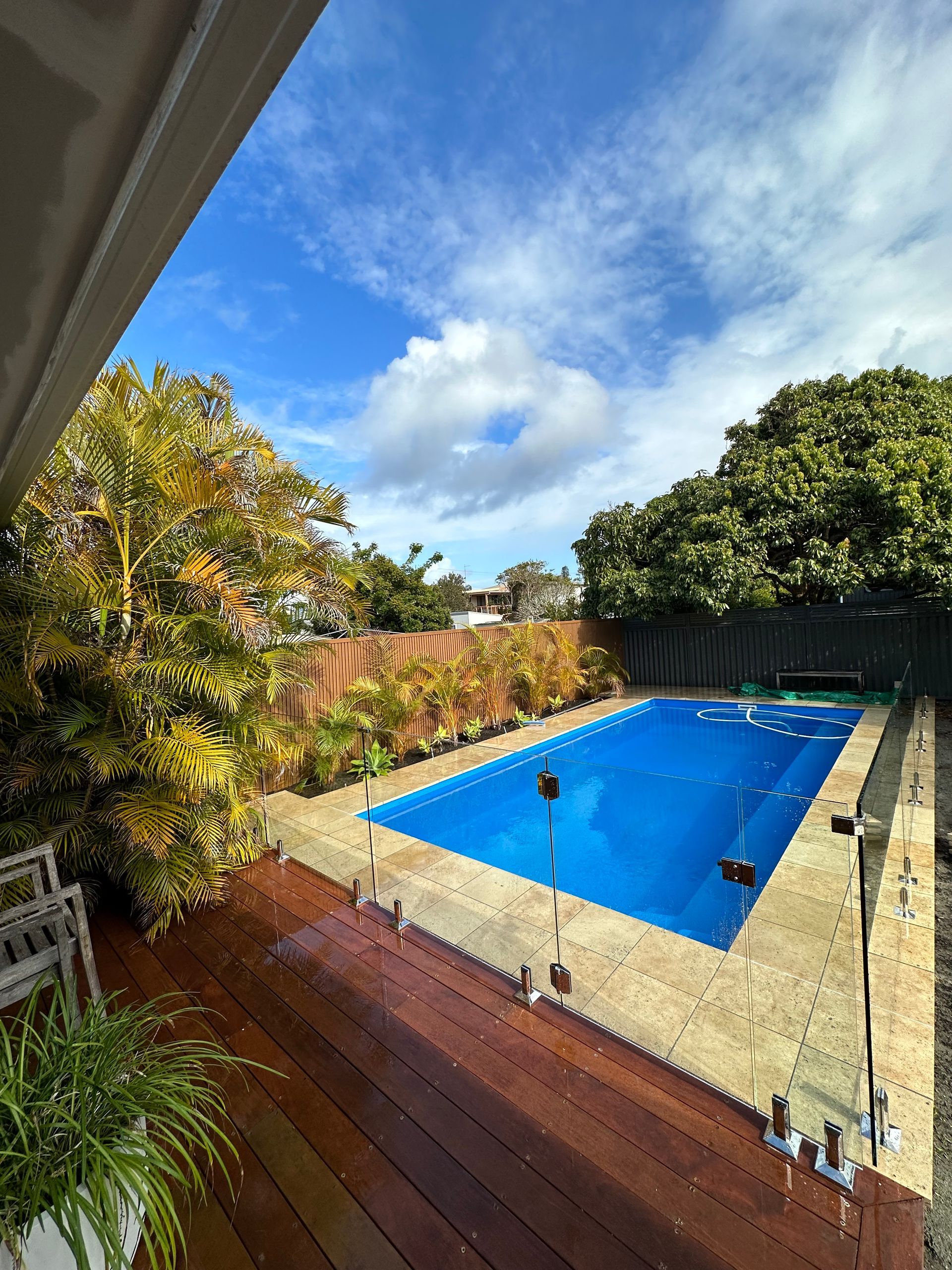 A large swimming pool is surrounded by trees and a wooden deck. — Glass Pool Fencing Australia in Old Bar, NSW