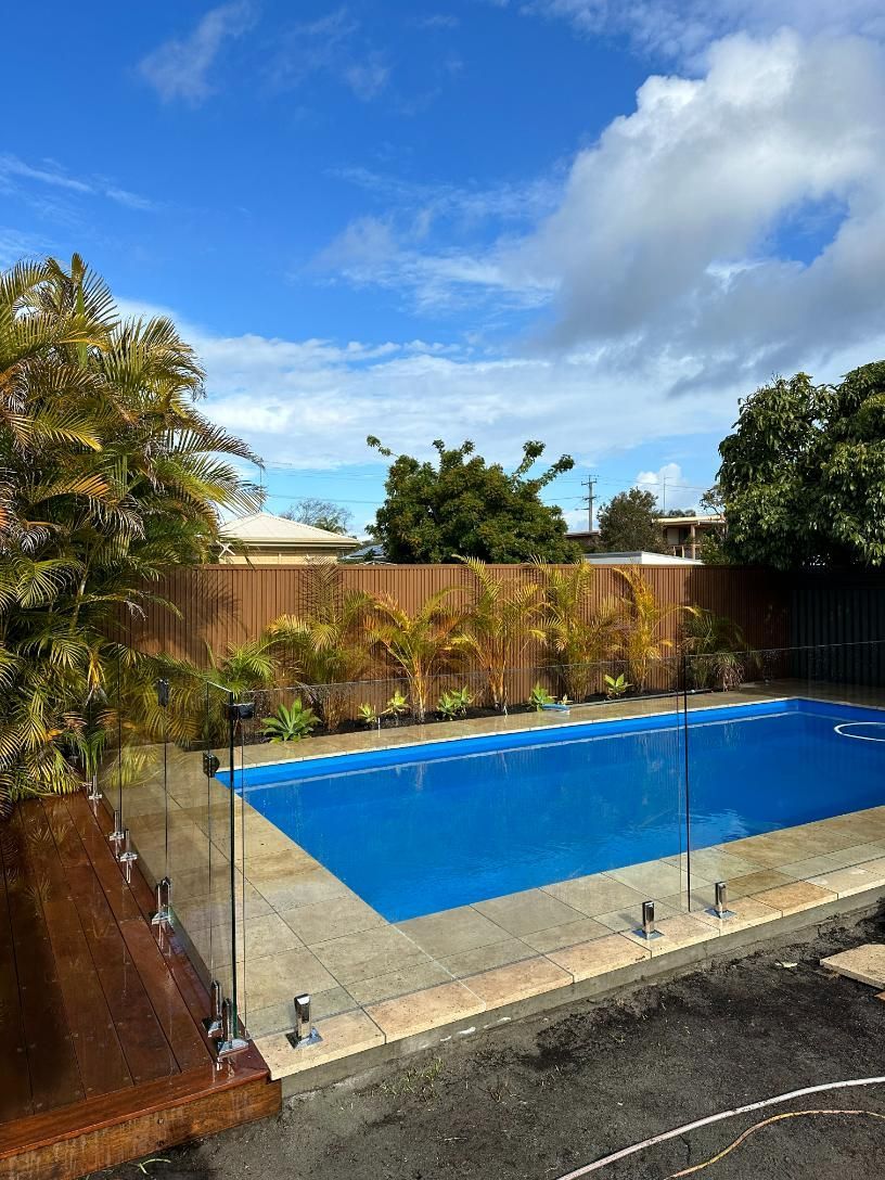 A Large Swimming Pool In A Backyard With A Glass Fence Surrounding It — Glass Pool Fencing Australia in Old Bar, NSW
