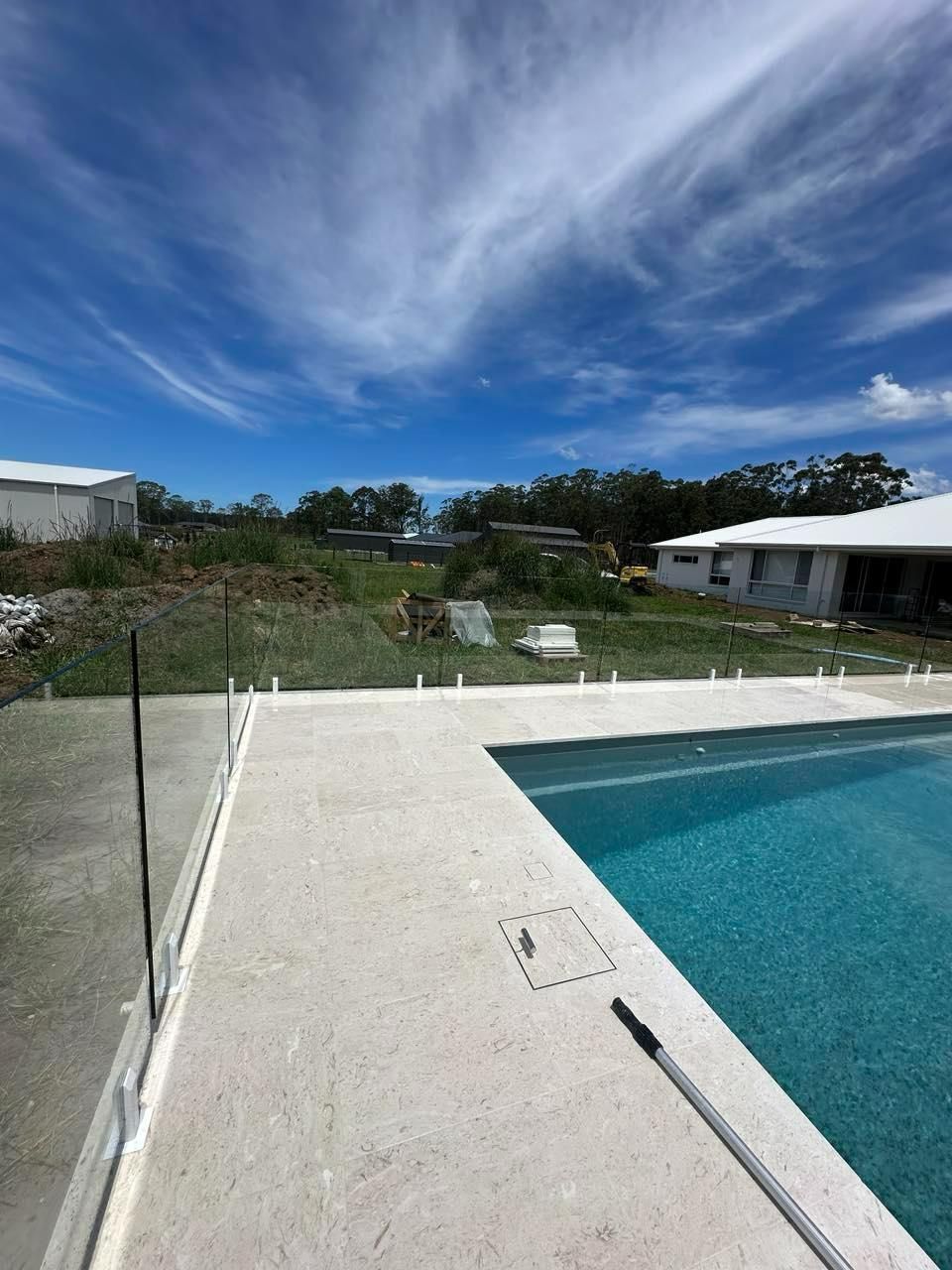 A Swimming Pool With A White House In The Background — Glass Pool Fencing Australia in Old Bar, NSW