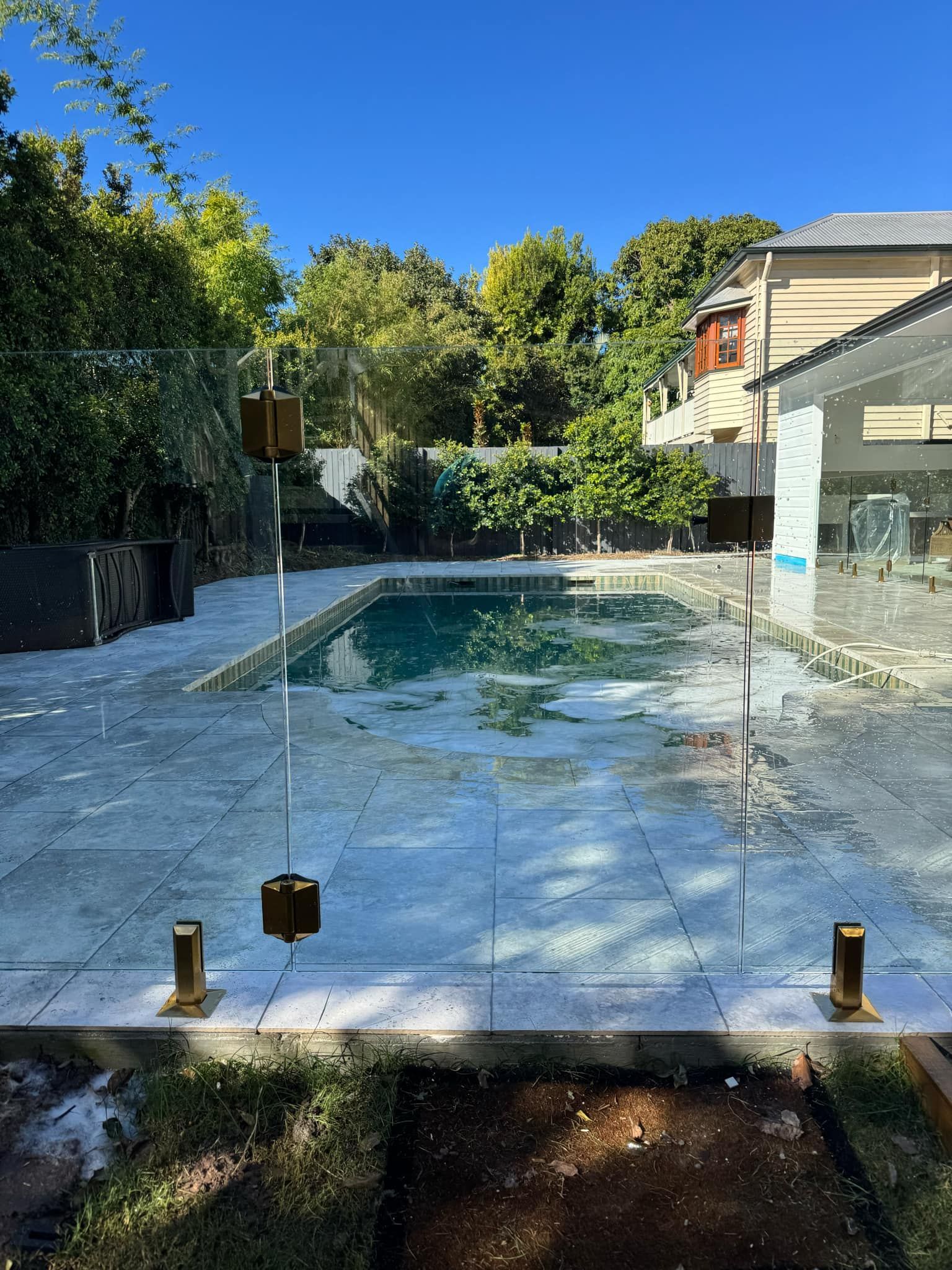 Glass Pool Fence Panels Standing on A Tiled Patio — Coastline Glass Pool Fencing in Old Bar, NSW