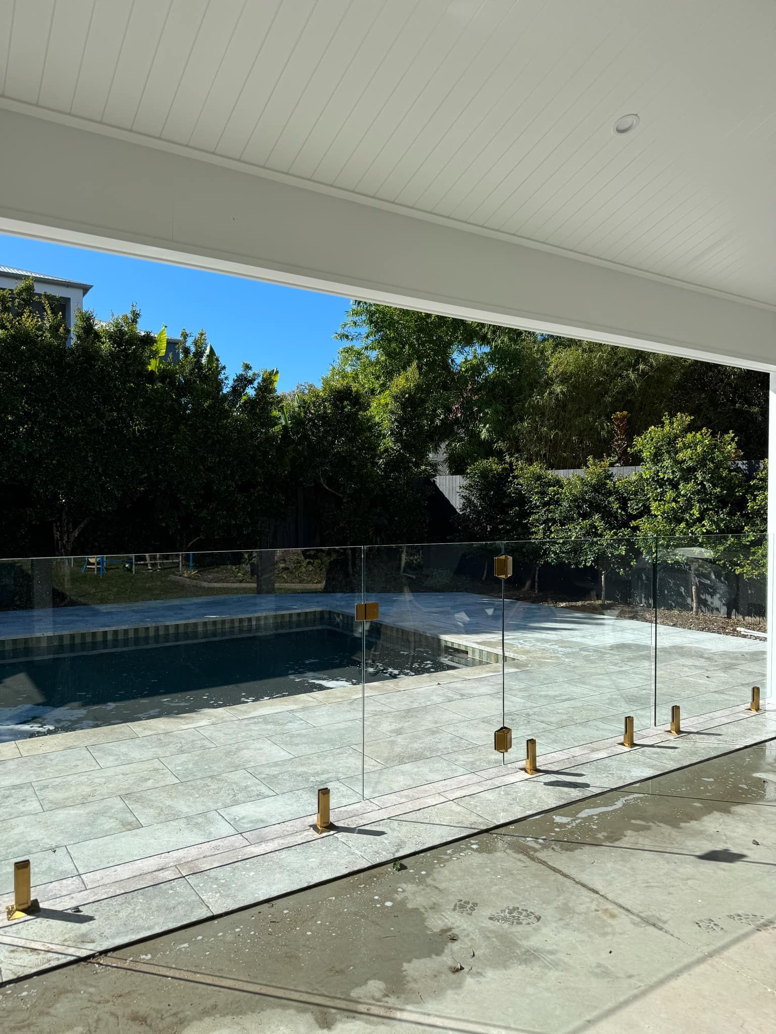 A Glass Pool Fence Borders a Paved Patio with A Swimming Pool — Coastline Glass Pool Fencing in Old Bar, NSW