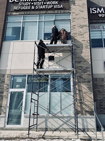 Three people work on a metal scaffolding platform installed in front of the second-story windows of a commercial building.