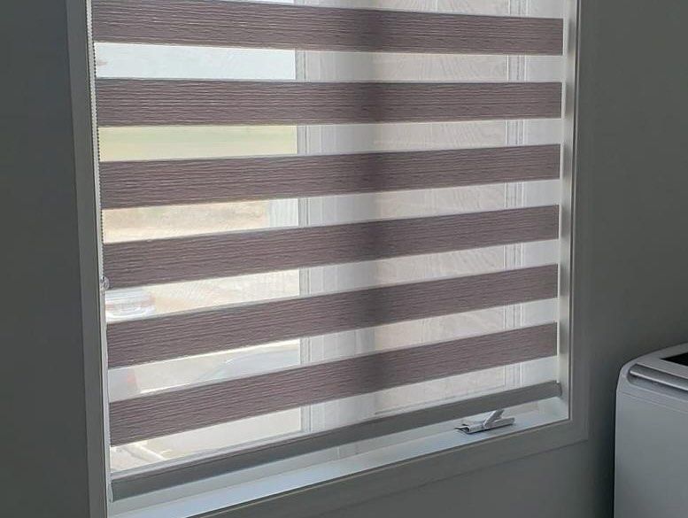 A window featuring beige and white striped zebra roller shades in a closed, light-filtering position.