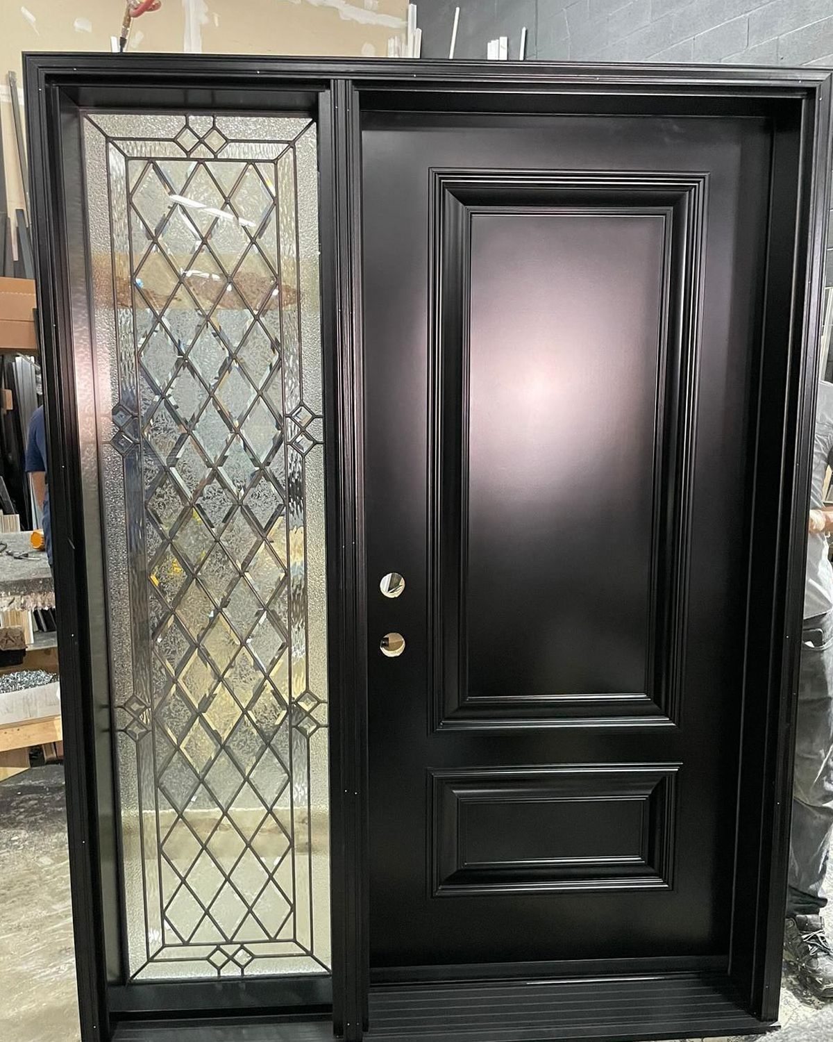 A black front door with a two-panel design next to a tall, side window featuring a decorative leaded glass diamond pattern.