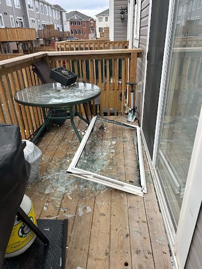 A shattered glass sliding door panel lies on a wooden deck next to a glass patio table.
