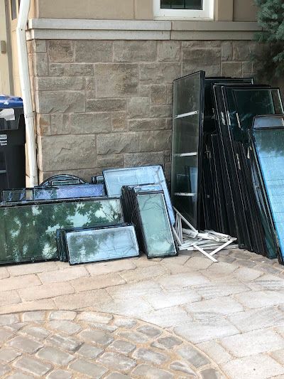 A collection of various glass window panels stacked against a stone house exterior.