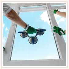 Two gloved hands hold a triple-suction cup tool against a large windowpane, installing or replacing a glass panel.