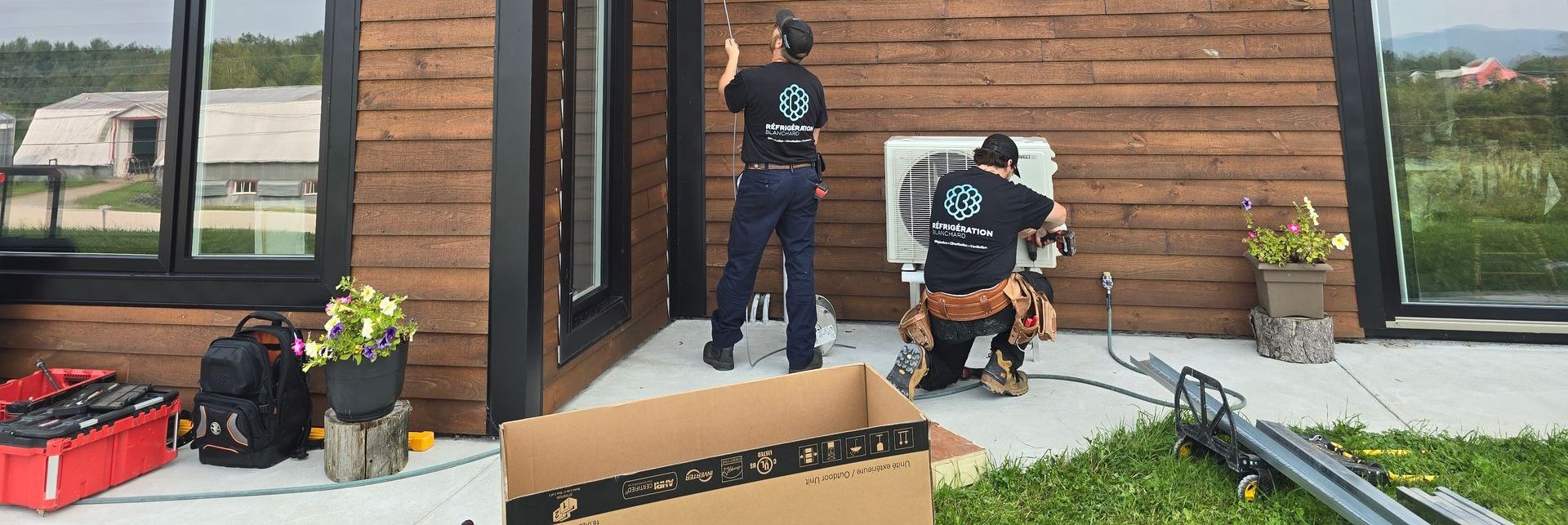 Deux hommes travaillent sur un climatiseur à l'extérieur d'une maison.