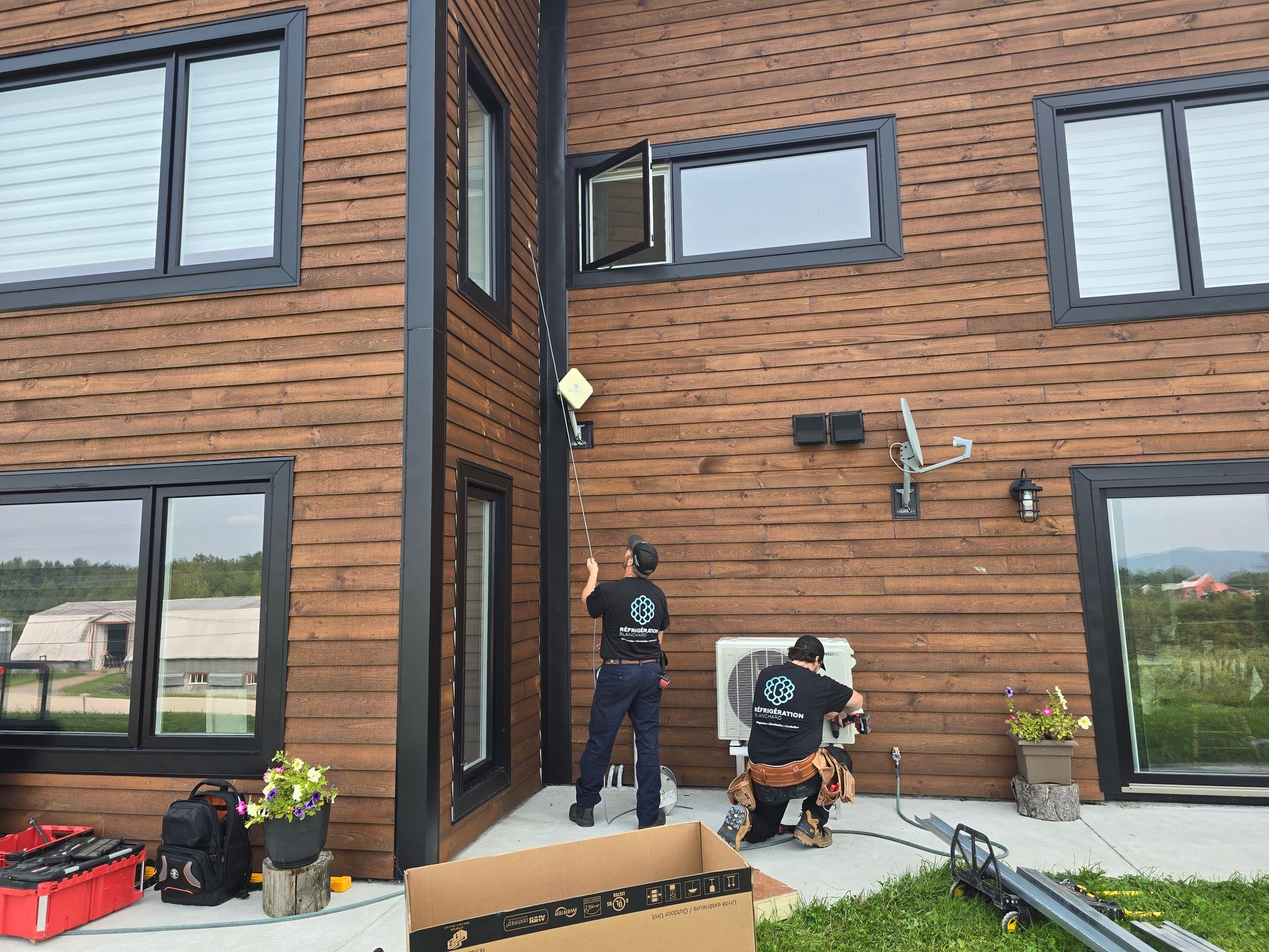 Deux hommes travaillent sur un climatiseur à l'extérieur d'une maison.