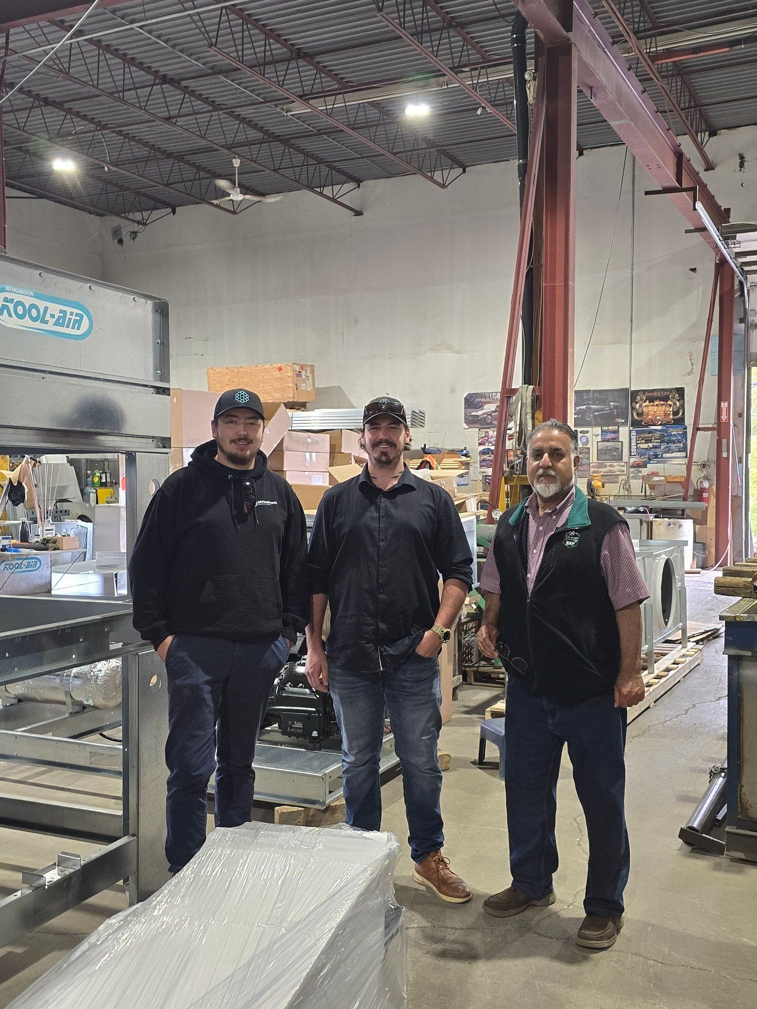 Trois hommes se tiennent côte à côte dans un entrepôt.