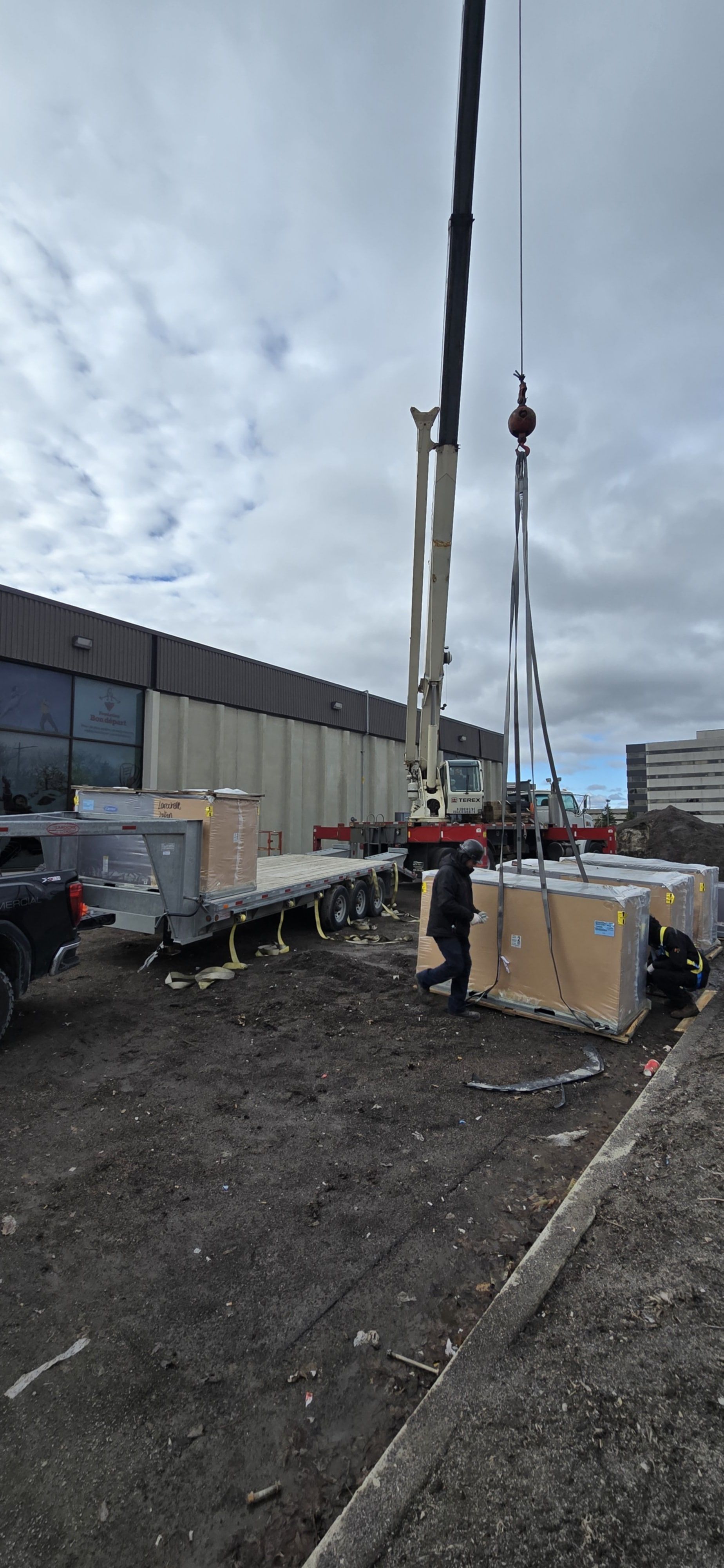 Une grue soulève une grande boîte dans un parking.