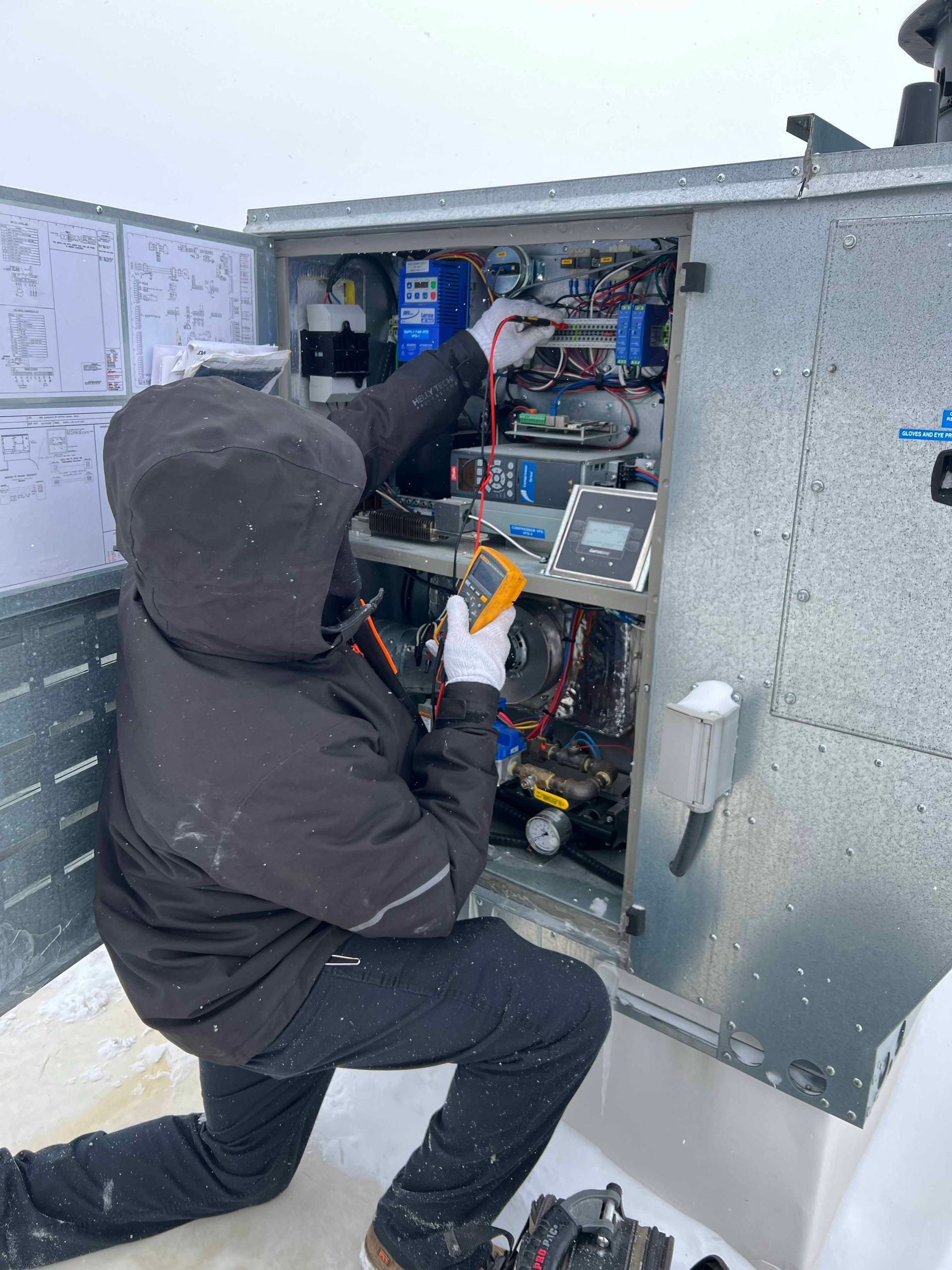 Un homme en veste noire travaille sur une machine dans la neige.