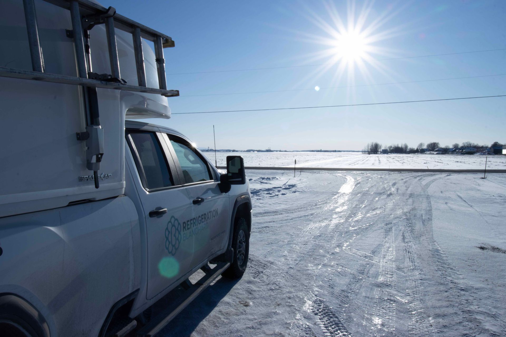 Un camion blanc est garé dans la neige par une journée ensoleillée.