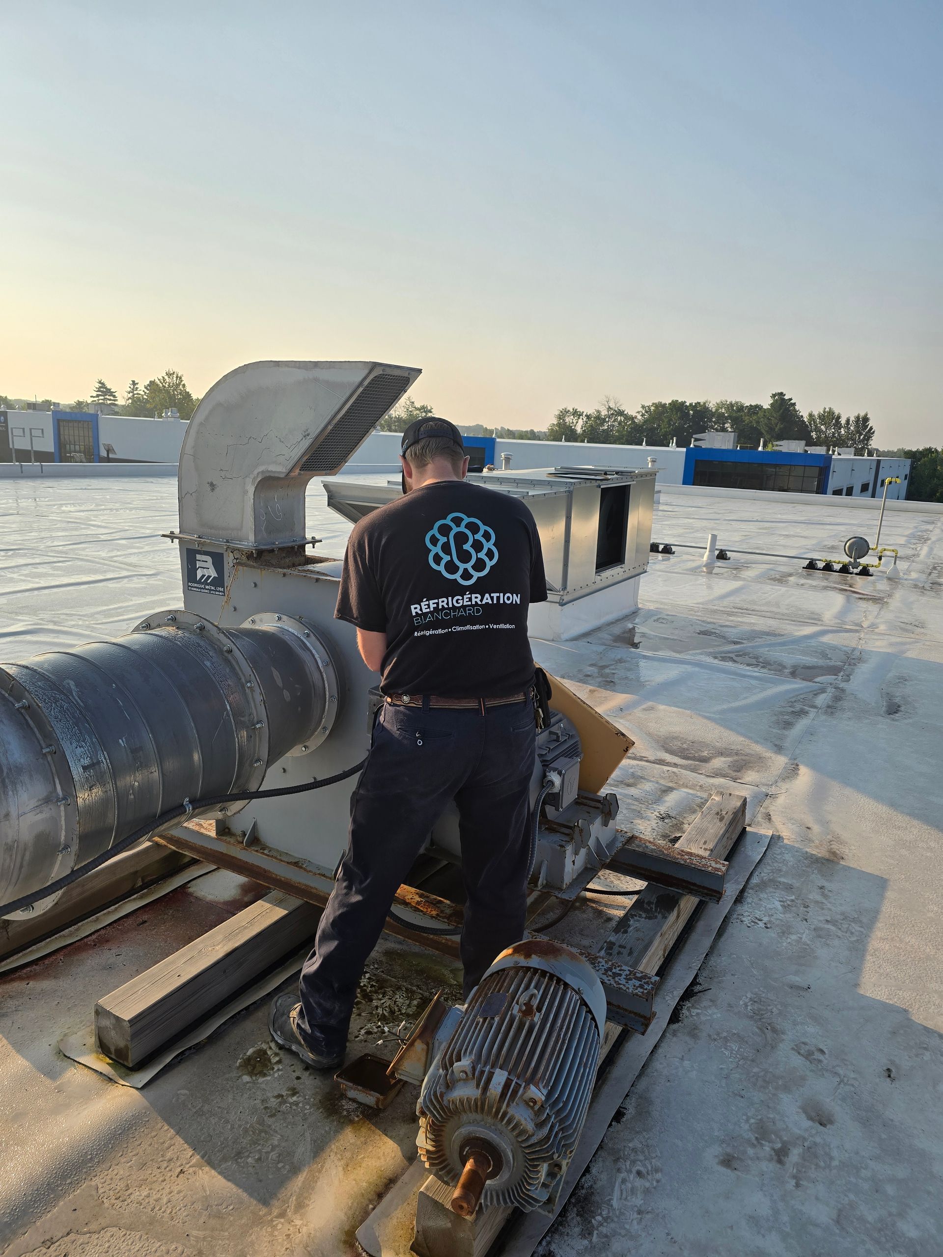 Un homme travaille sur un ventilateur au sommet d'un toit.