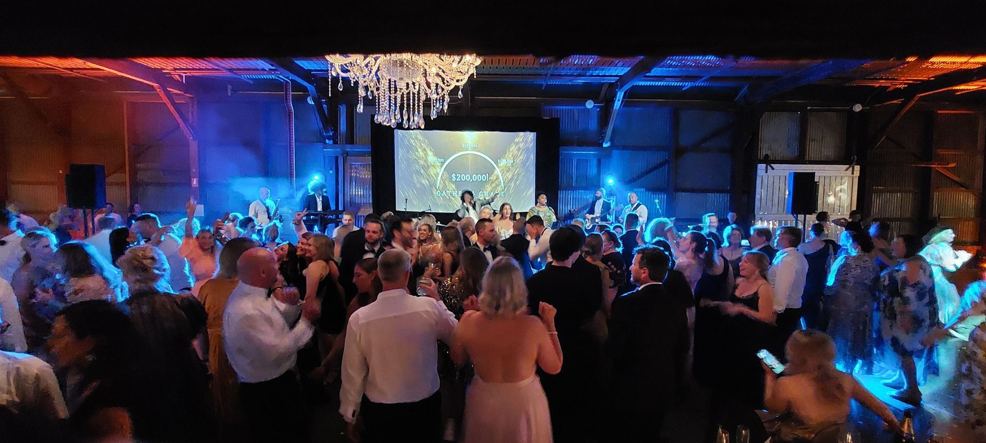 A large group of people are dancing at a party in a large room.
