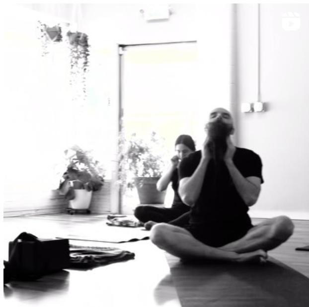 Students in group meditation wearing black in a room with plants