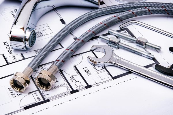 Chrome plumbing fixtures and flexible hoses laid on top of architectural blueprints.