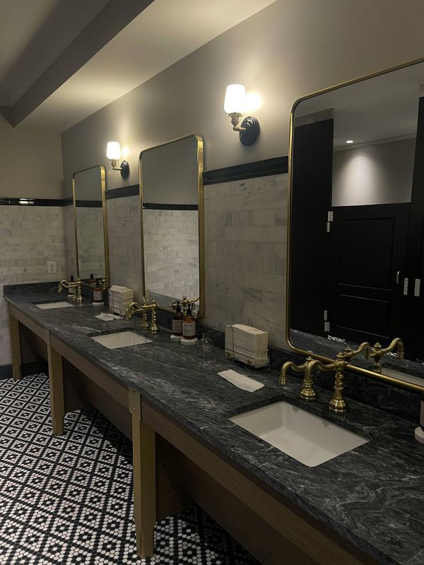 Elegant restroom with long granite sink counter, mirrors, wall sconces, and patterned tile floor