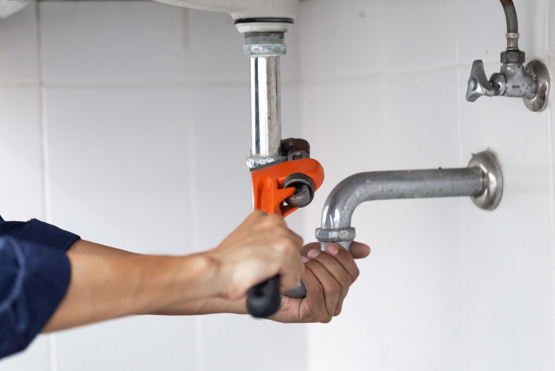 A plumber is fixing a sink pipe with a wrench.