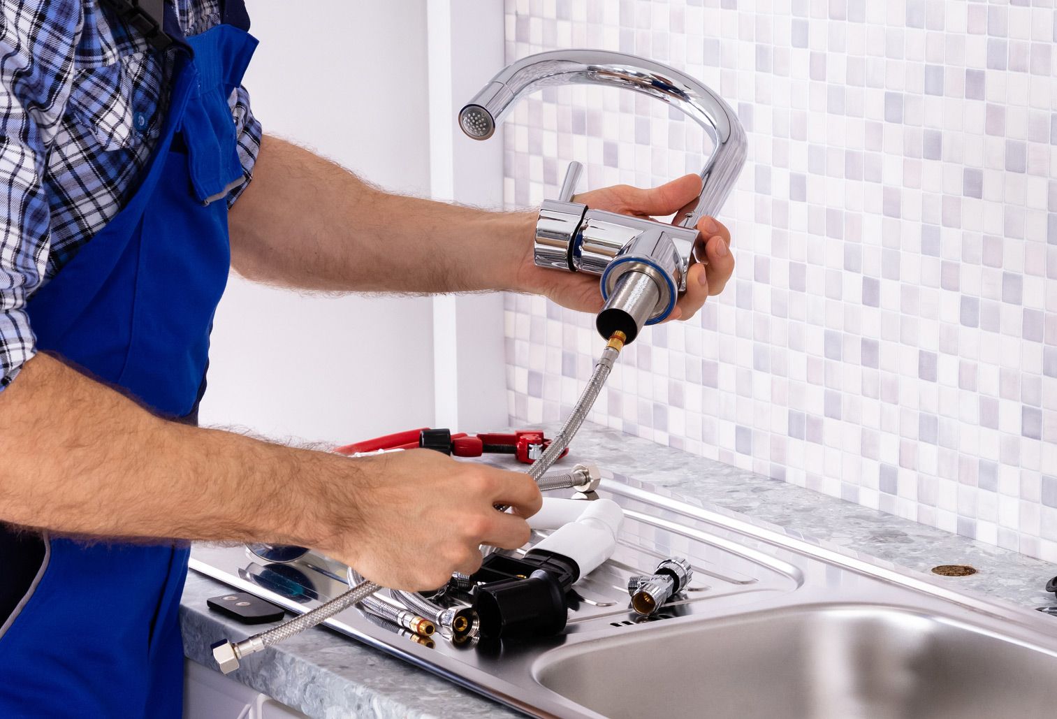 A plumber is fixing a faucet in a kitchen.
