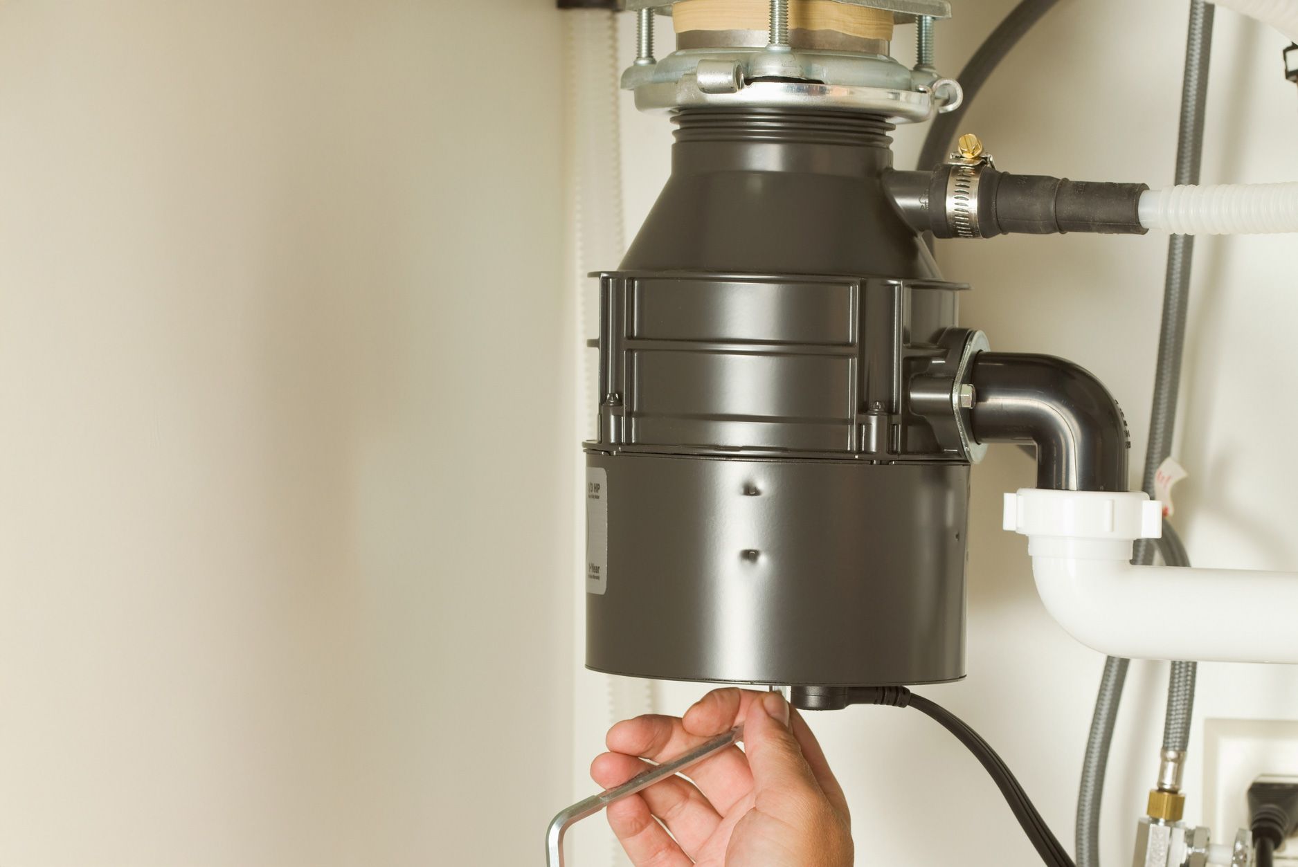A person is fixing a garbage disposal with a wrench.