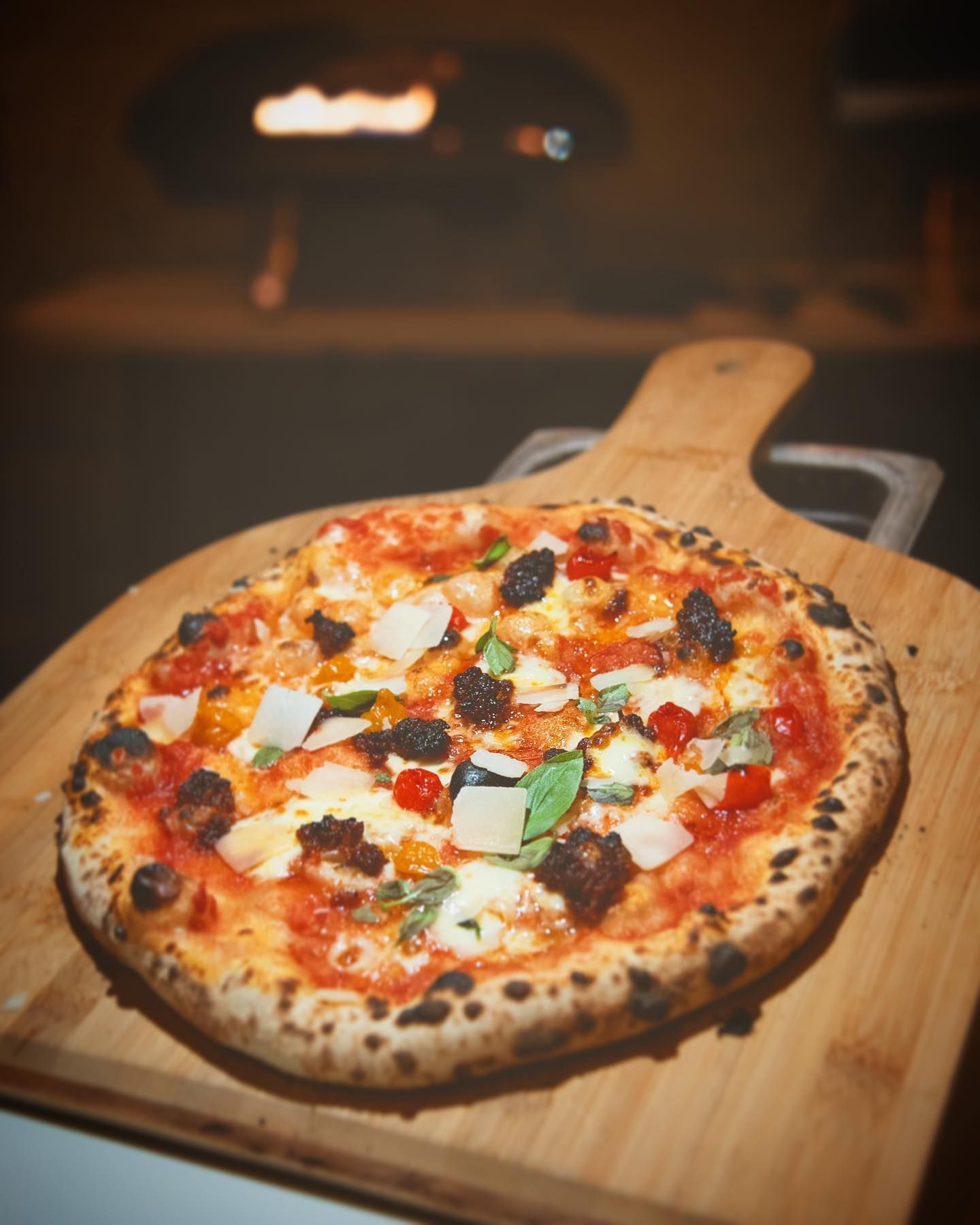 'Nduja pizza with parmigiano shavings in front of a pizza oven
