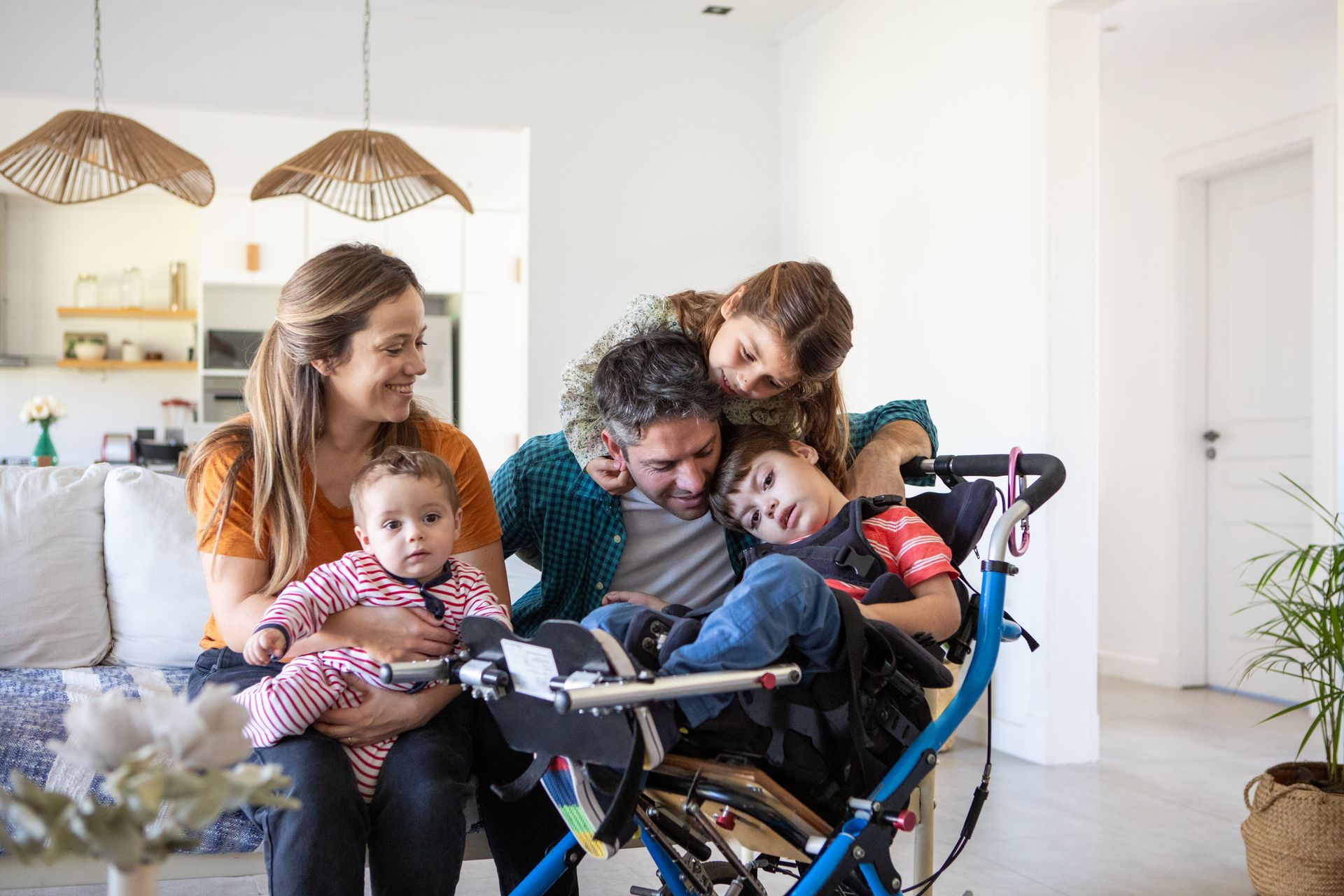 A family gathers around a child in a wheelchair, sharing a warm, affectionate embrace in a bright living room.