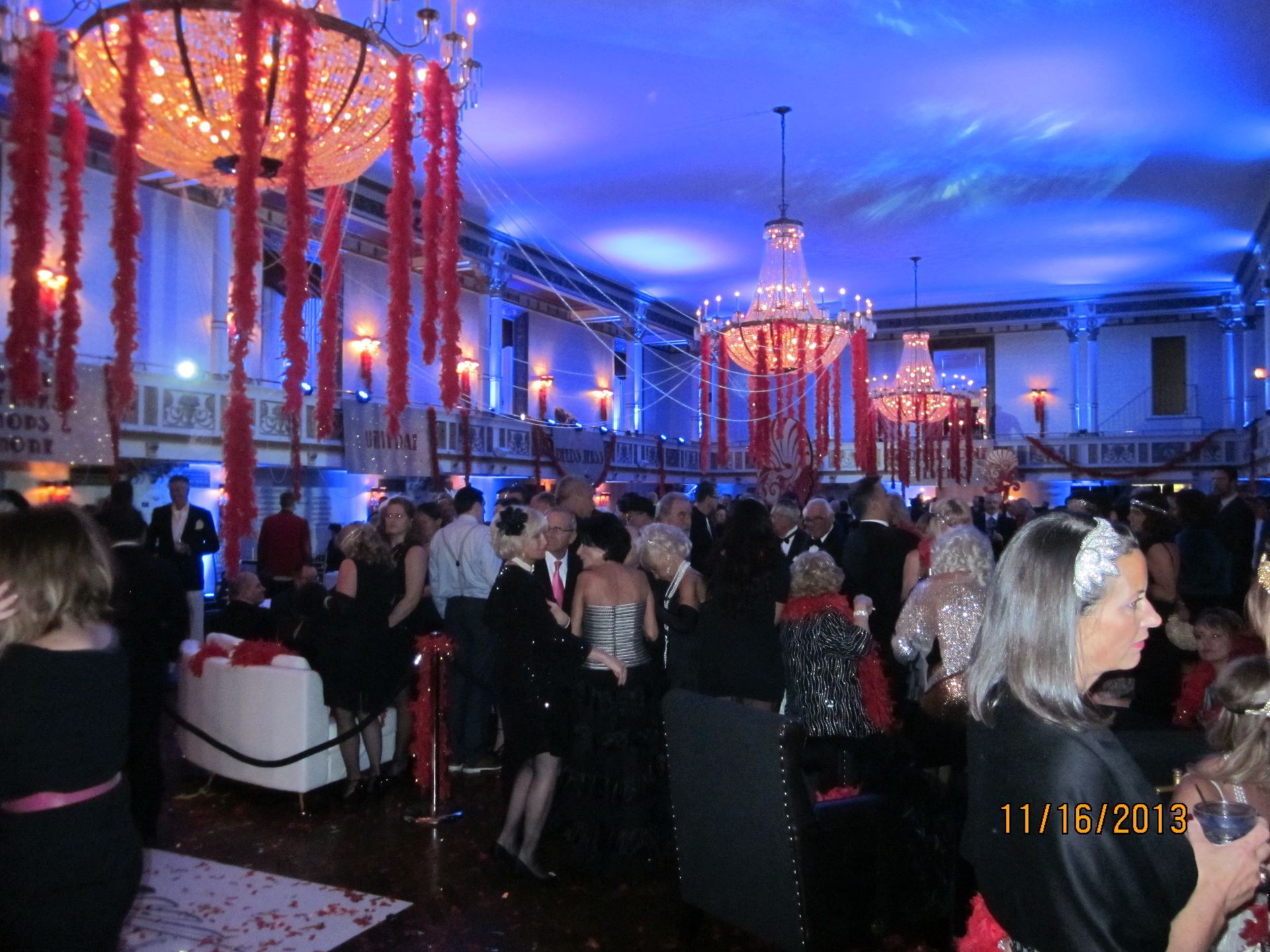 A crowd of people are gathered in a large room with a chandelier hanging from the ceiling