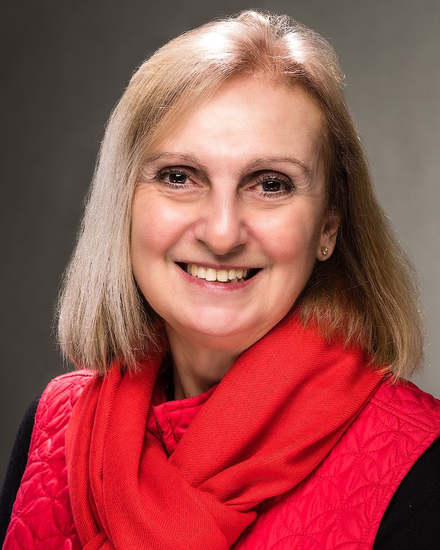 A woman wearing a red scarf and a red vest is smiling for the camera.