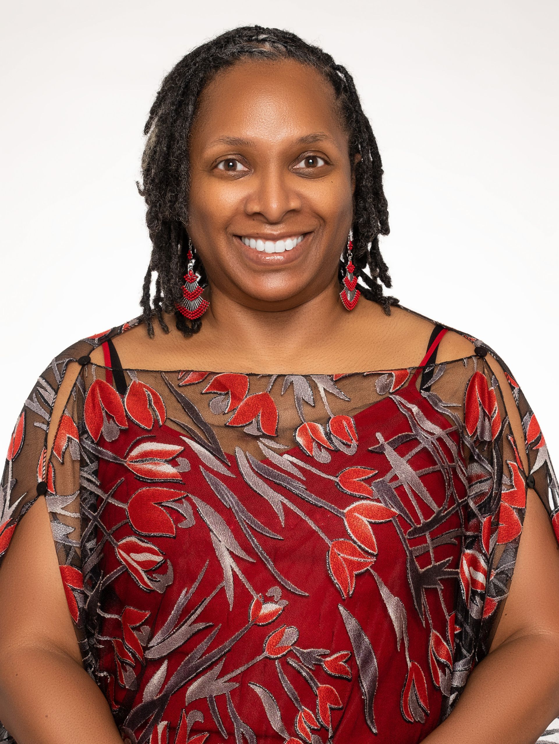 A woman wearing a red top and earrings is smiling for the camera.