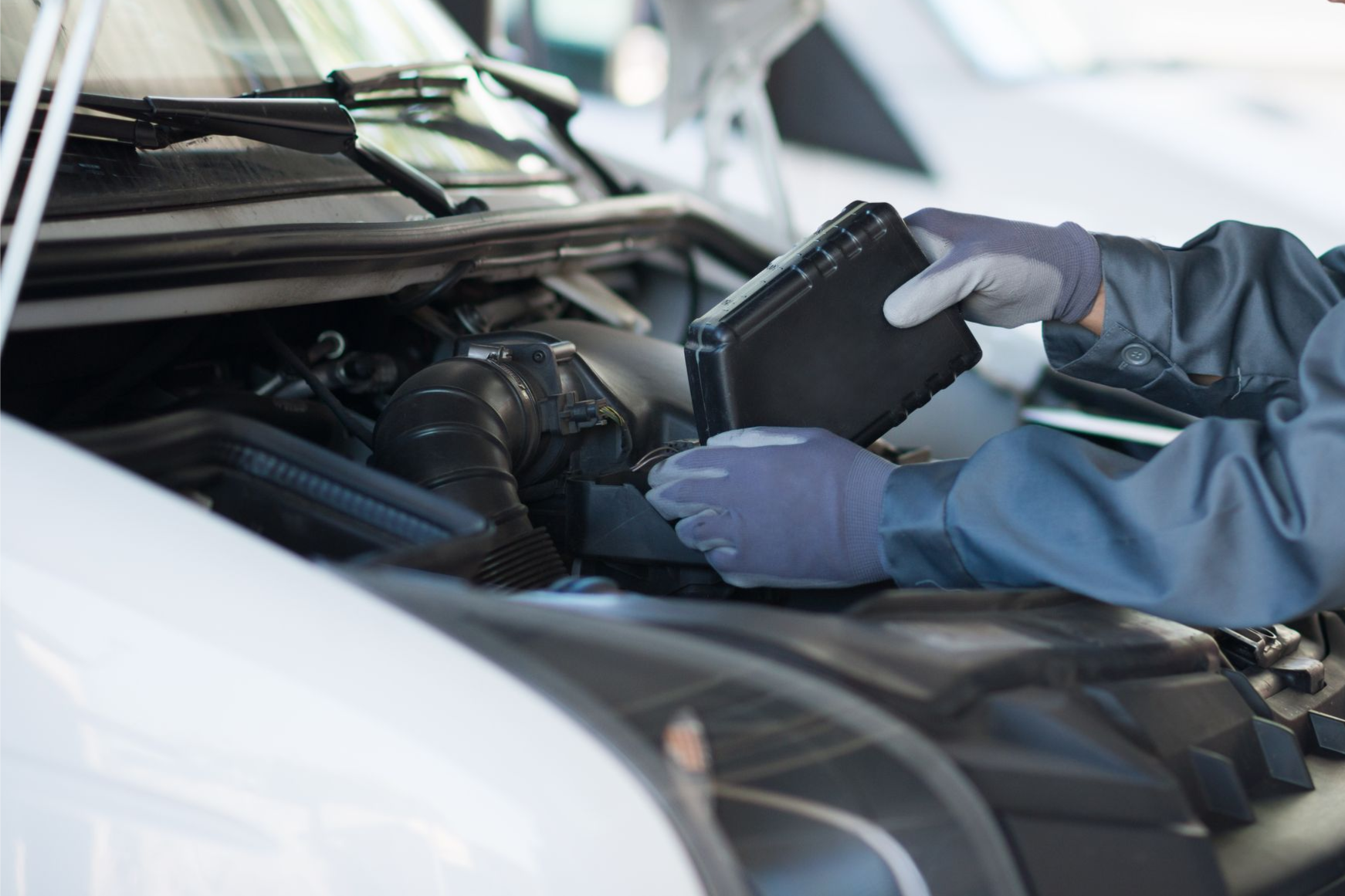 Ein Mechaniker mit Handschuhen überprüft mit einem Diagnosegerät den Motor eines Autos unter der geöffneten Motorhaube.