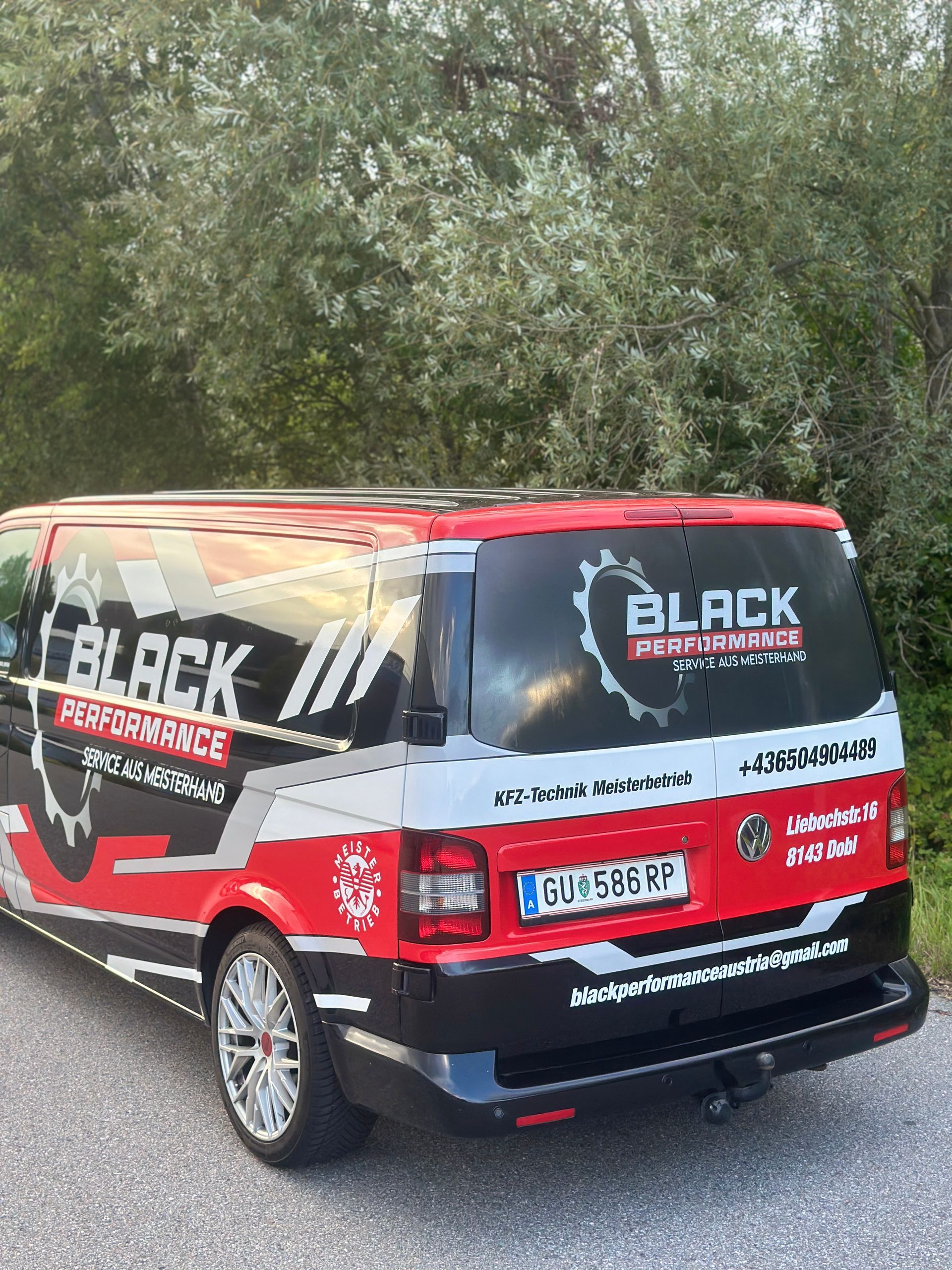 Roter und schwarzer Versicherungswagen, im Freien neben Bäumen geparkt, Seiten- und Rückansicht