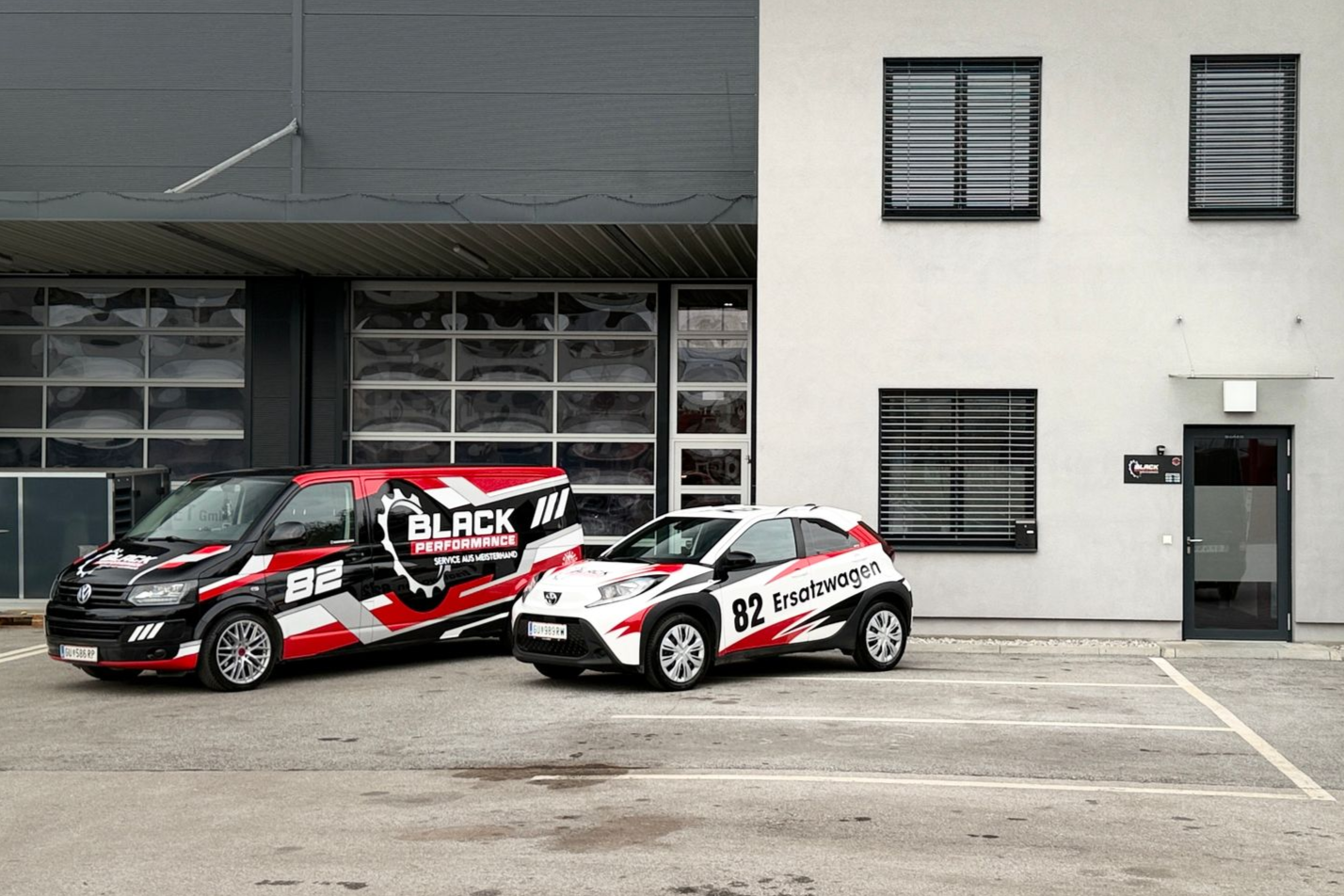 Zwei rot-weiß-schwarze Rennwagen parkten vor einem grauen Garagengebäude.