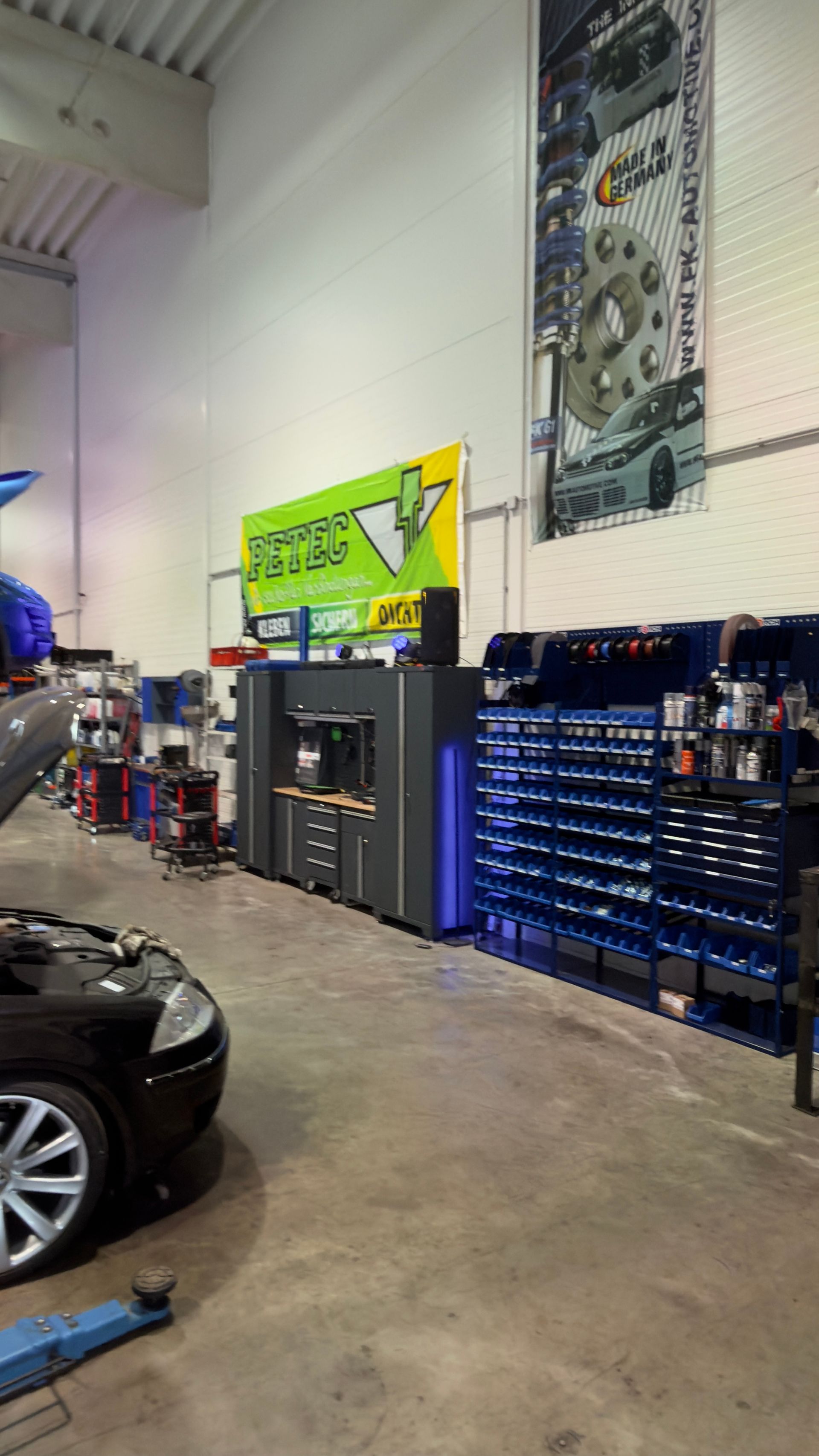 Innenansicht einer Autowerkstatt mit blauen Werkzeugschränken, einem Auto und Wandpostern