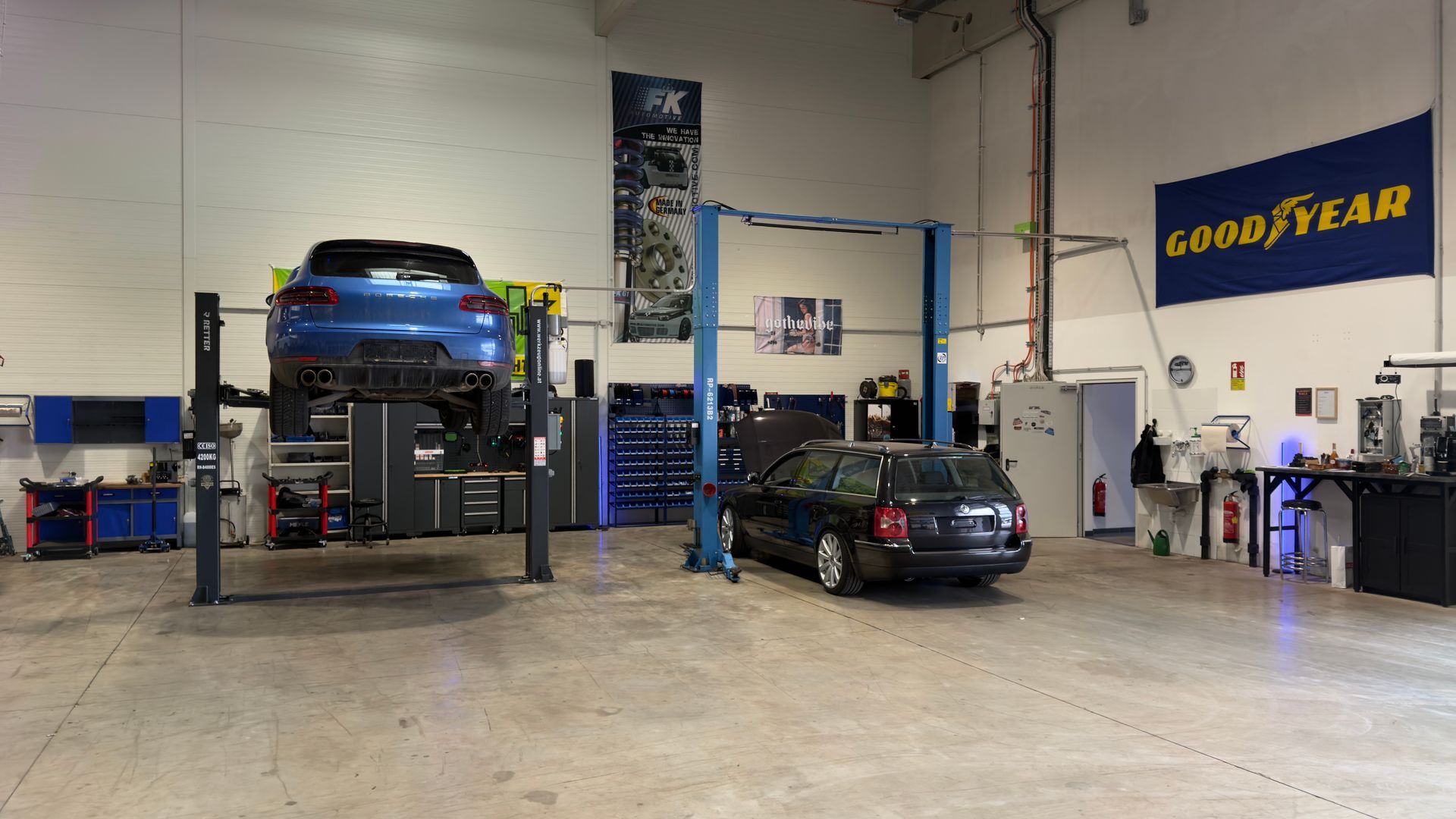 Autowerkstatt mit einem blauen Auto auf der Hebebühne und einem schwarzen Auto auf dem Boden