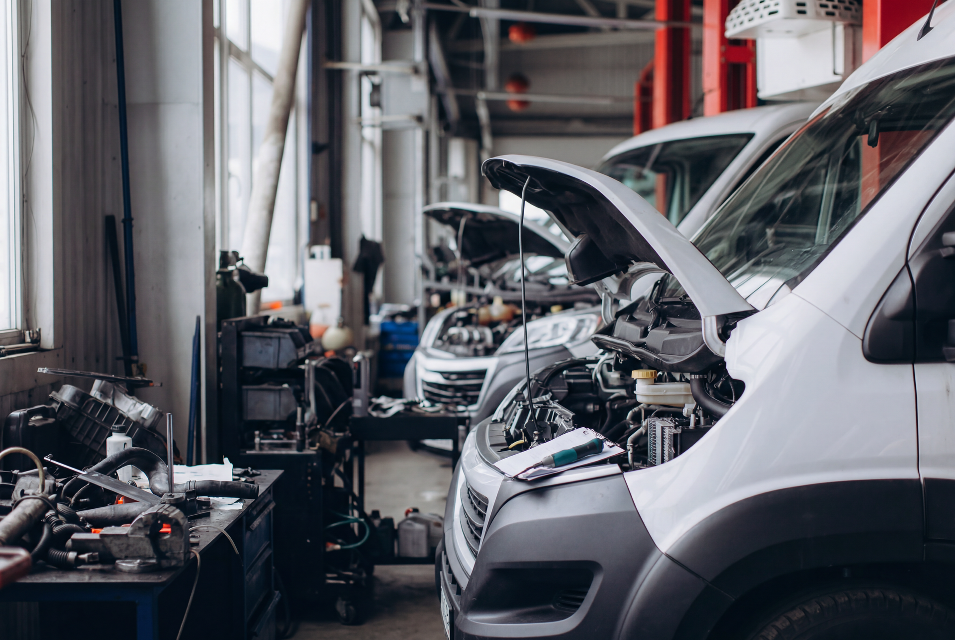 Autowerkstatt mit mehreren in Wartung befindlichen Autos, eine Motorhaube ist geöffne