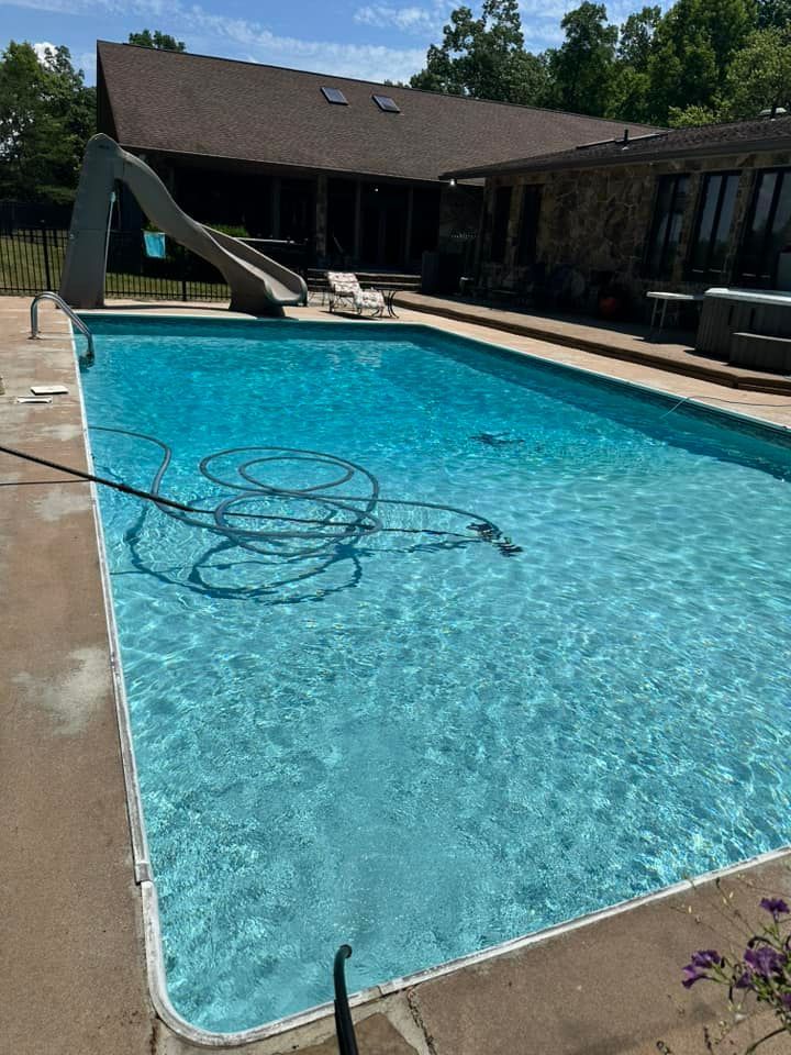Rectangular swimming pool with slide next to a house with a brown roof on a sunny day.