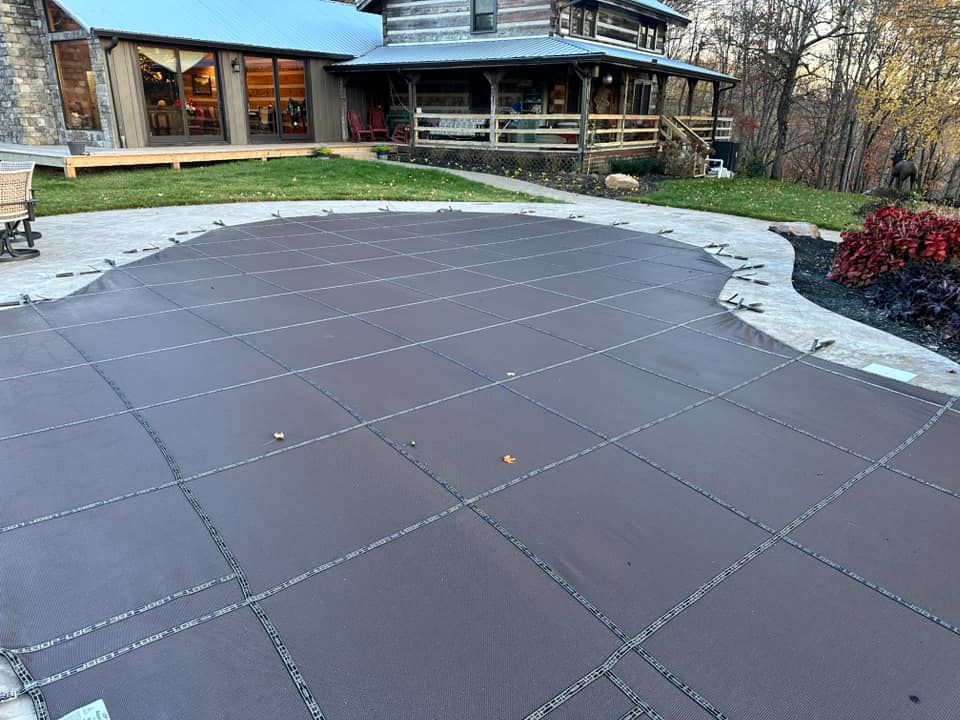 A dark brown pool cover over an in-ground pool in front of a log cabin with a porch.