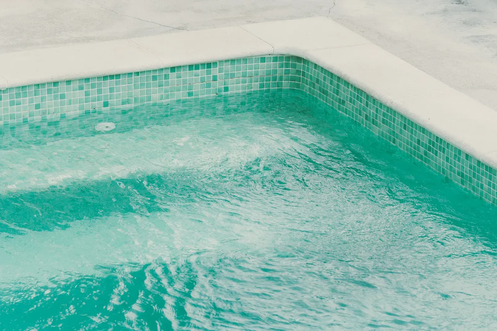 Turquoise water ripples in a tiled pool, edge with white trim.