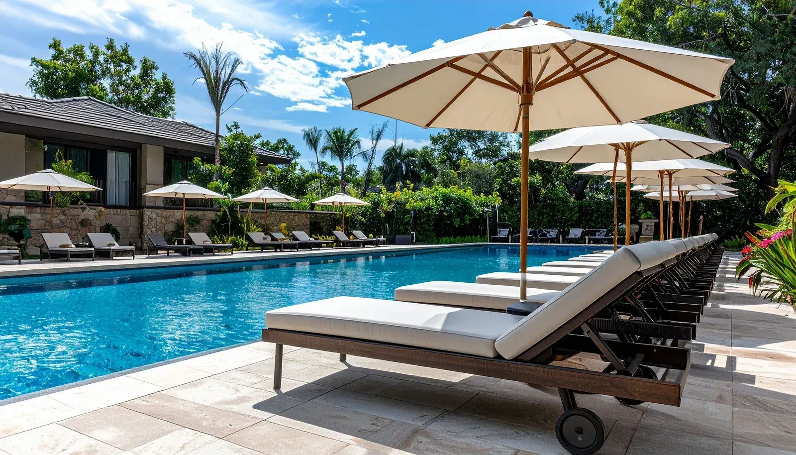 Swimming pool with lounge chairs, umbrellas, and a building on a sunny day.