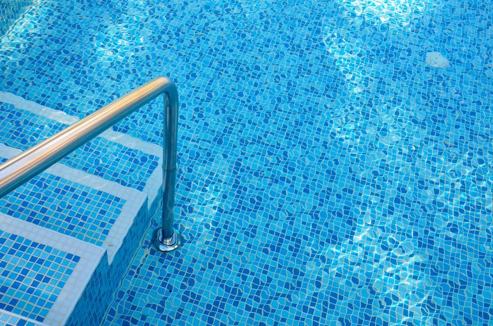 Swimming pool with blue tile and stainless steel handrail over steps.