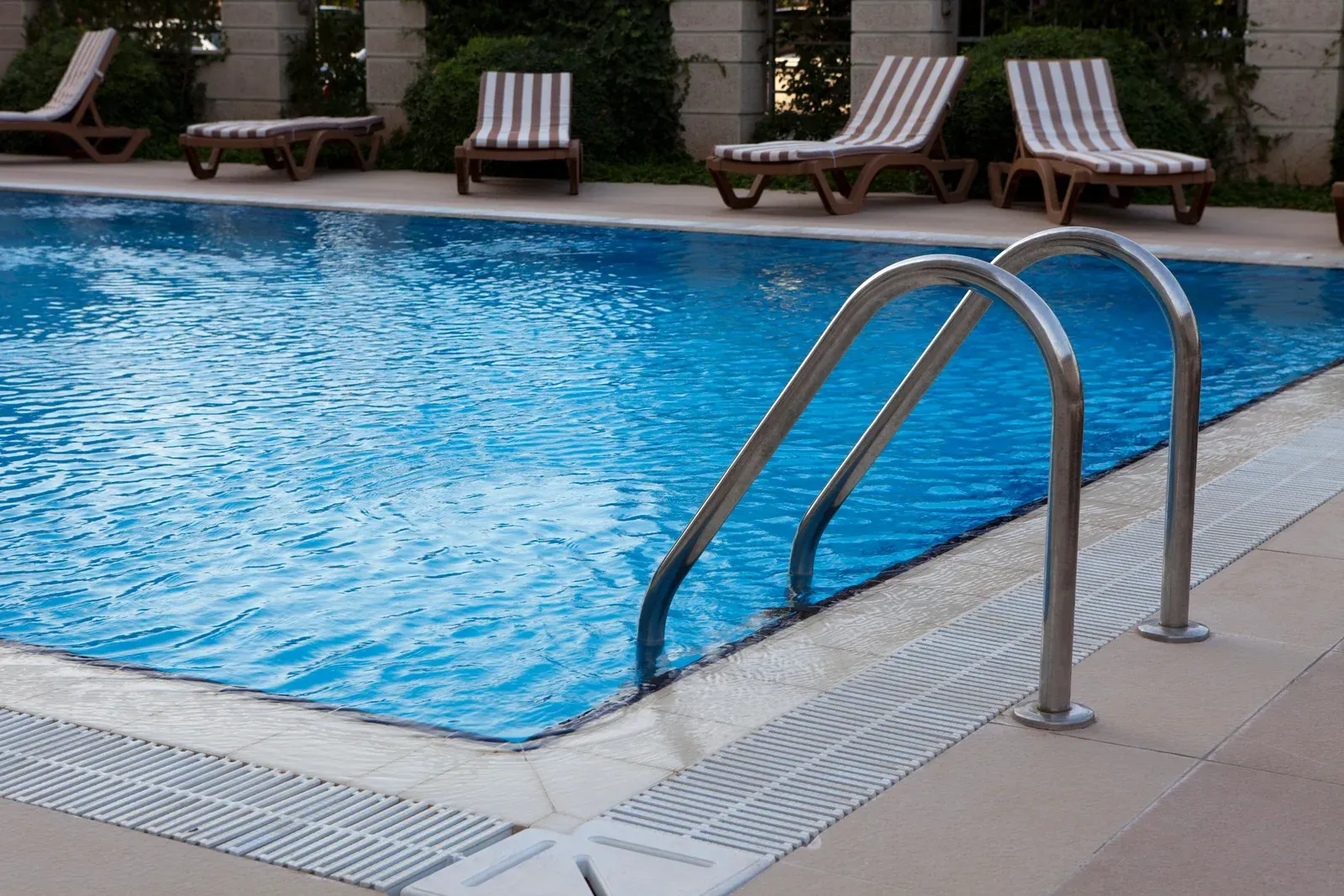 Swimming pool with metal ladder, blue water, and lounge chairs.