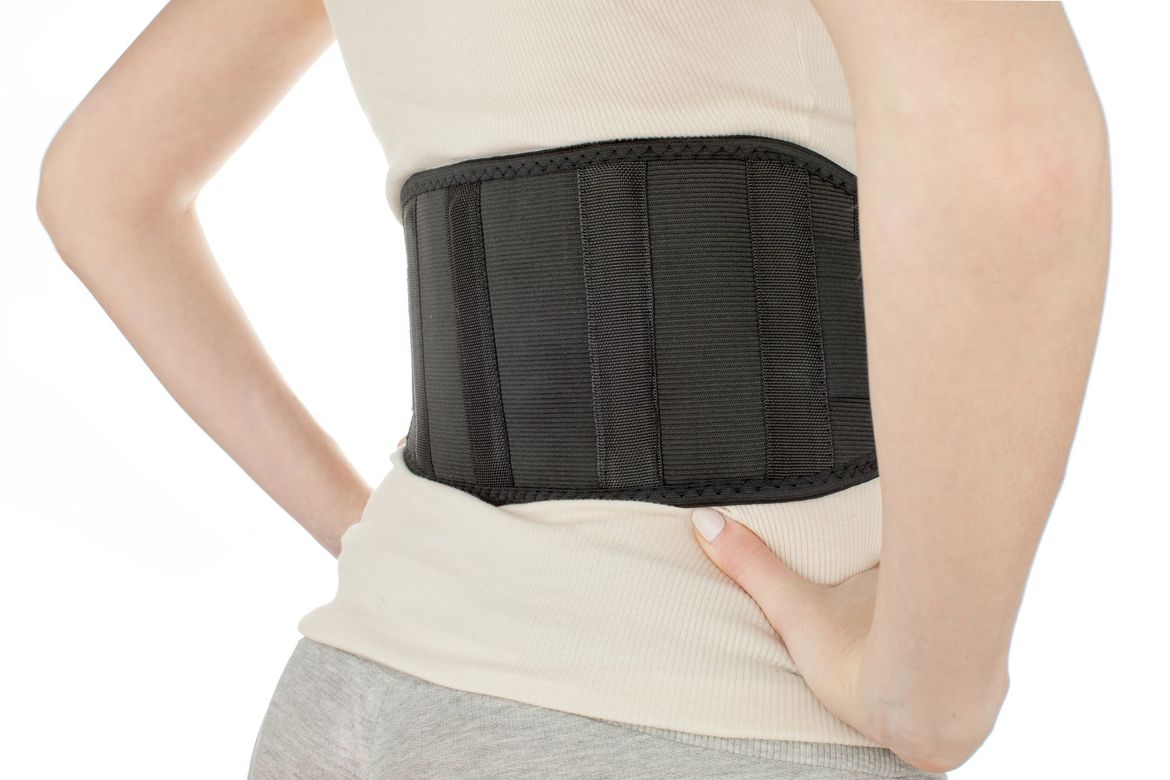Una persona indossa un corsetto di supporto lombare nero sopra una camicia chiara, con le mani appoggiate sui fianchi.