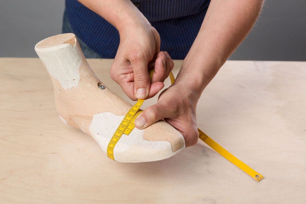 Delle mani usano un metro a nastro giallo per misurare la circonferenza di una forma per scarpe