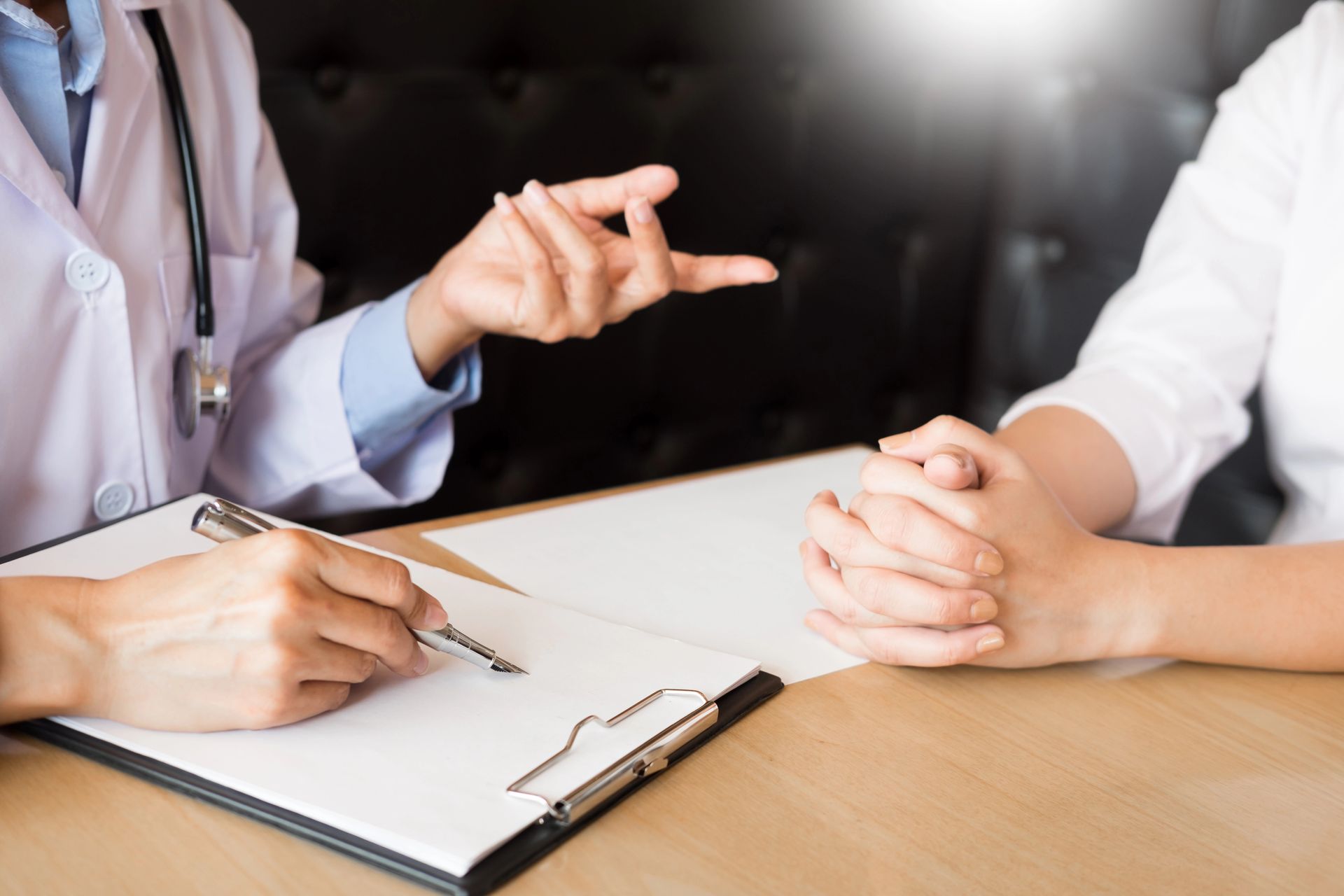 Un operatore sanitario in camice bianco gesticola mentre discute gli appunti presi su una cartella clinica con un paziente seduto.
