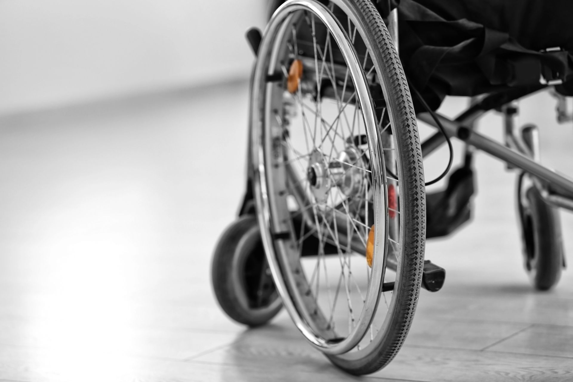 Vista laterale di una sedia a rotelle manuale su un pavimento chiaro, con particolare attenzione alla ruota a raggi e al telaio.