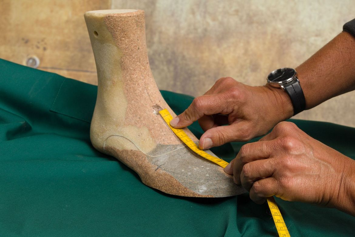 Delle mani utilizzano un metro a nastro giallo per misurare una forma di scarpa beige a forma di piede 