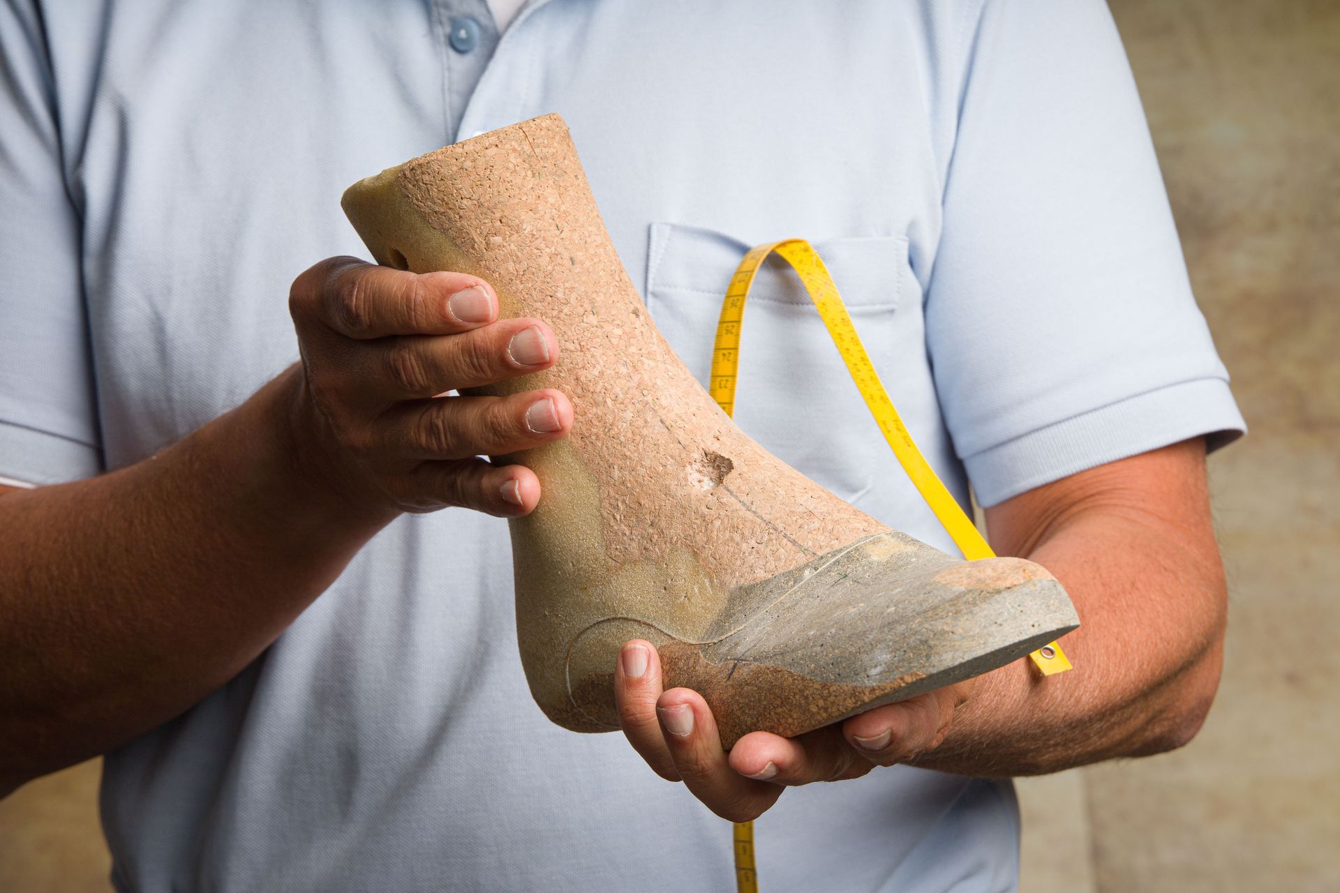 Una persona con una camicia azzurra tiene in mano una forma per scarpe beige
